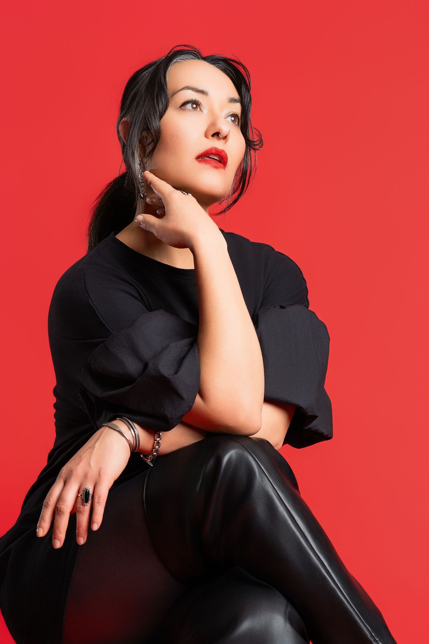 Dramatic portrait in black outfit against bold red background with artistic lighting.
