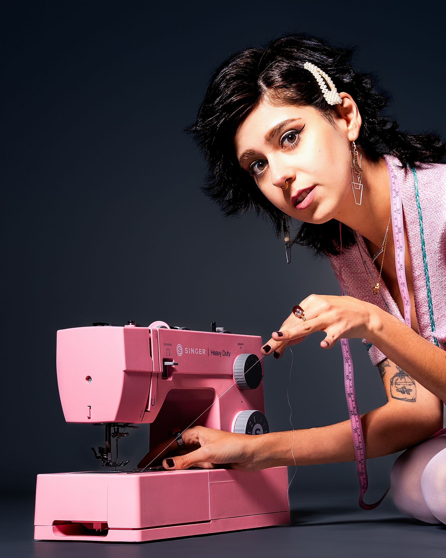 A pink vintage sewing machine is shown against a dark background with a person using it in retro-styled photography.