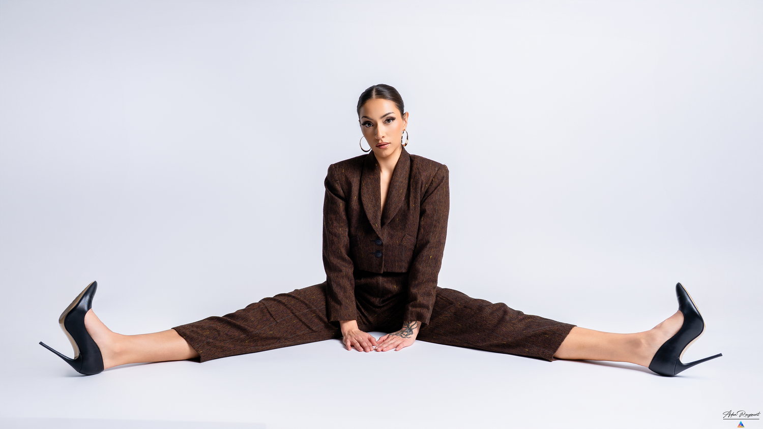 Model in brown business suit demonstrates impressive split pose on white background.