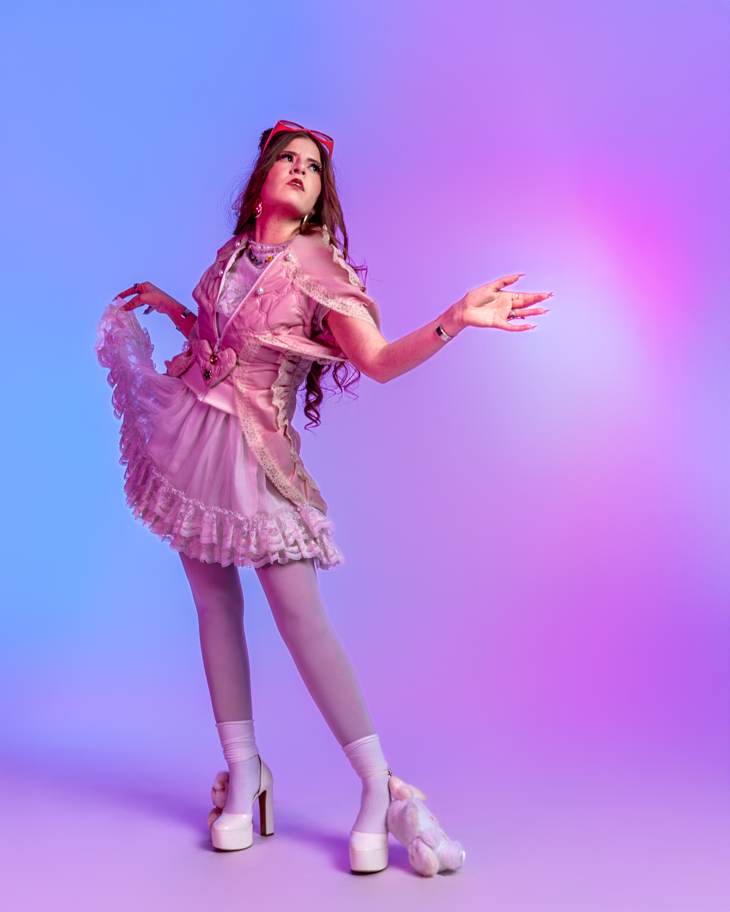Dancer in pink lolita-style dress performs expressive movements against colorful backdrop.