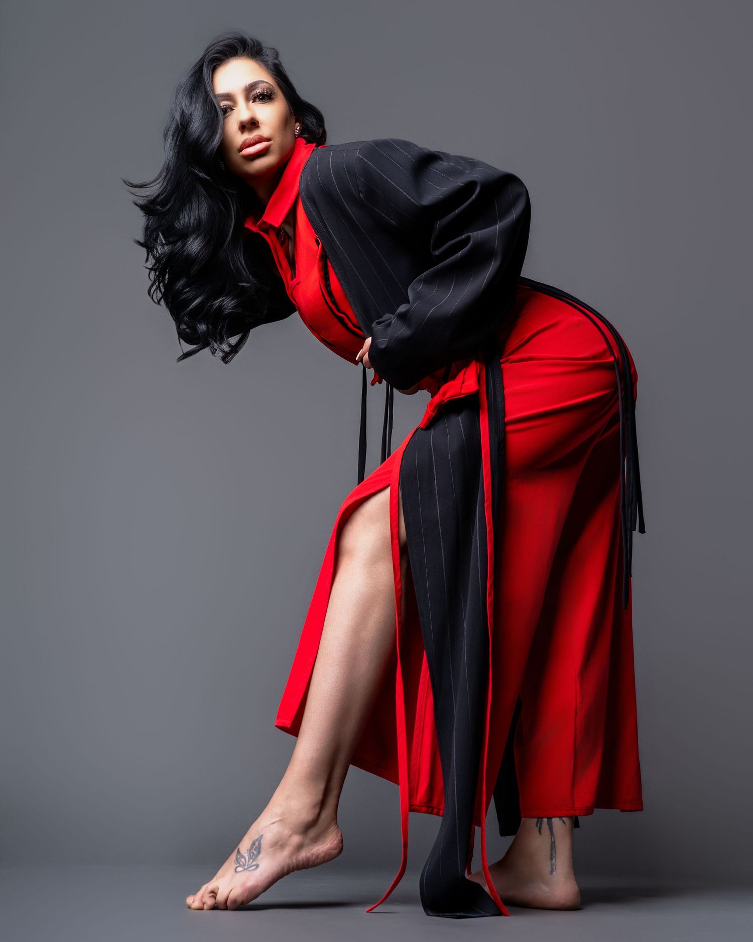 Dramatic fashion pose in flowing red and black ensemble against grey background.