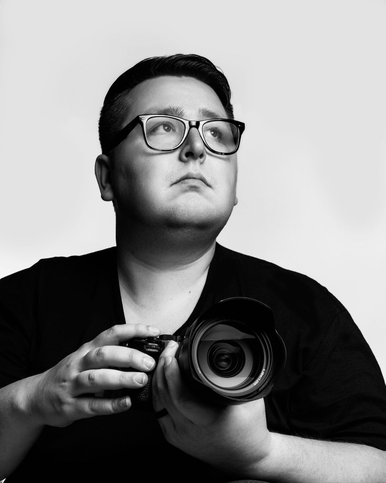 Black and white portrait of photographer holding professional camera with upward gaze.
