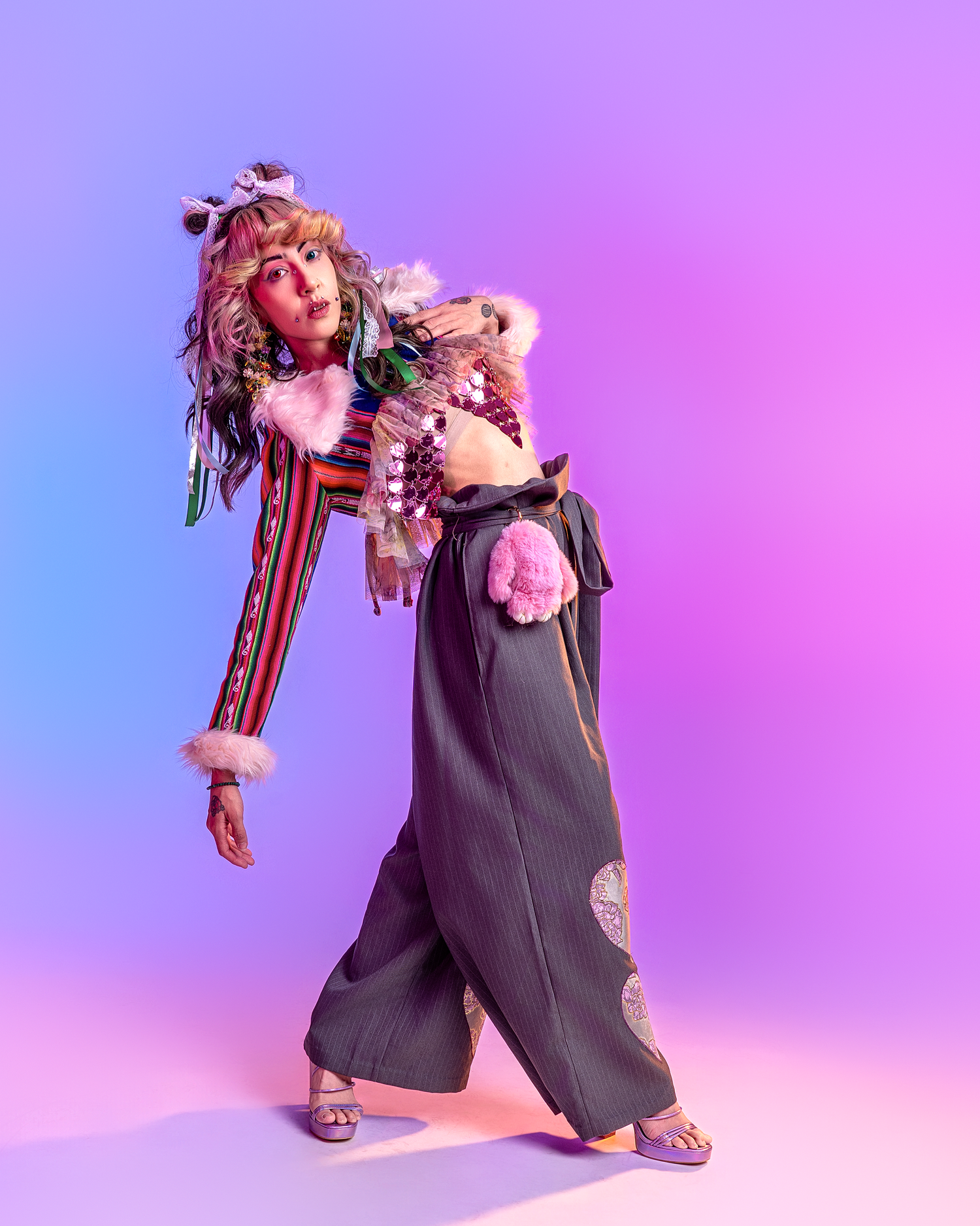Artistic fashion shot of figure in baggy overalls and pink accessories on purple gradient backdrop.