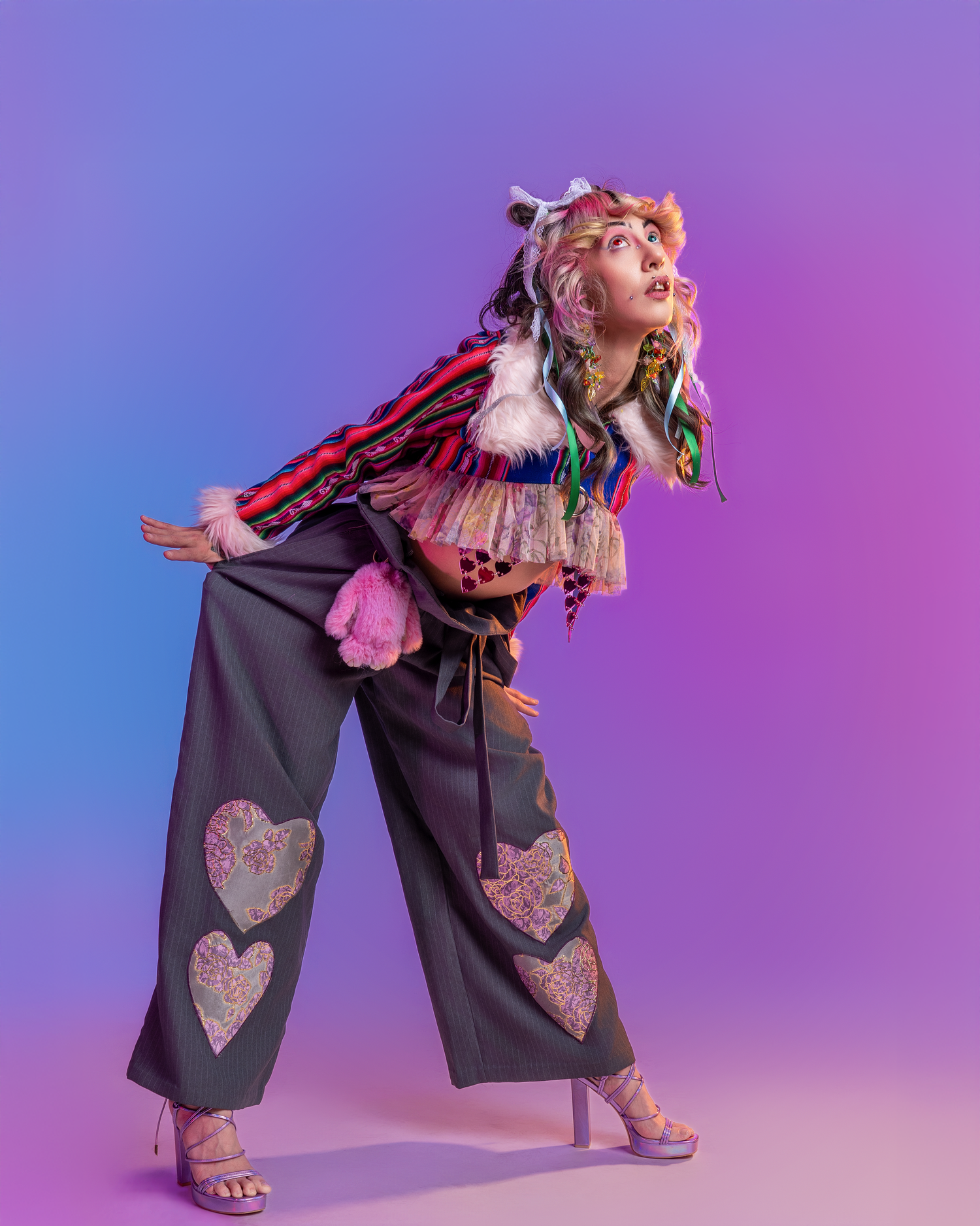 Fashion model poses in wide-leg navy pants with heart patches against purple gradient background.