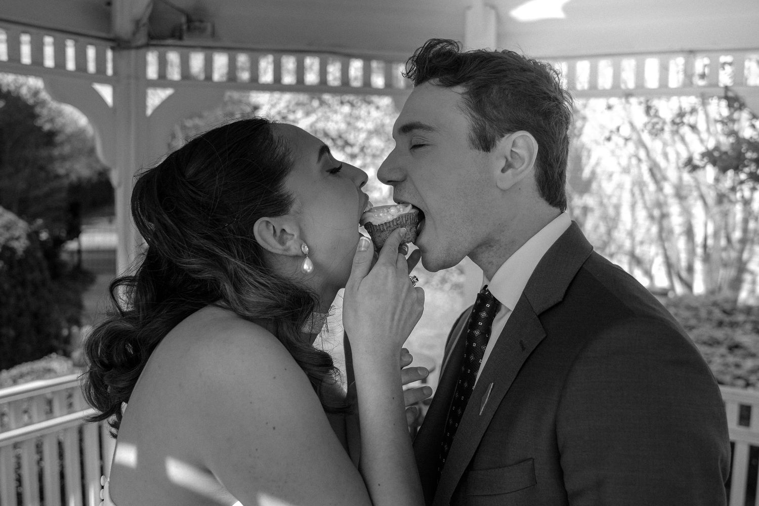 Black and white photo of a bride and groom sharing wedding cake at their reception ceremony.