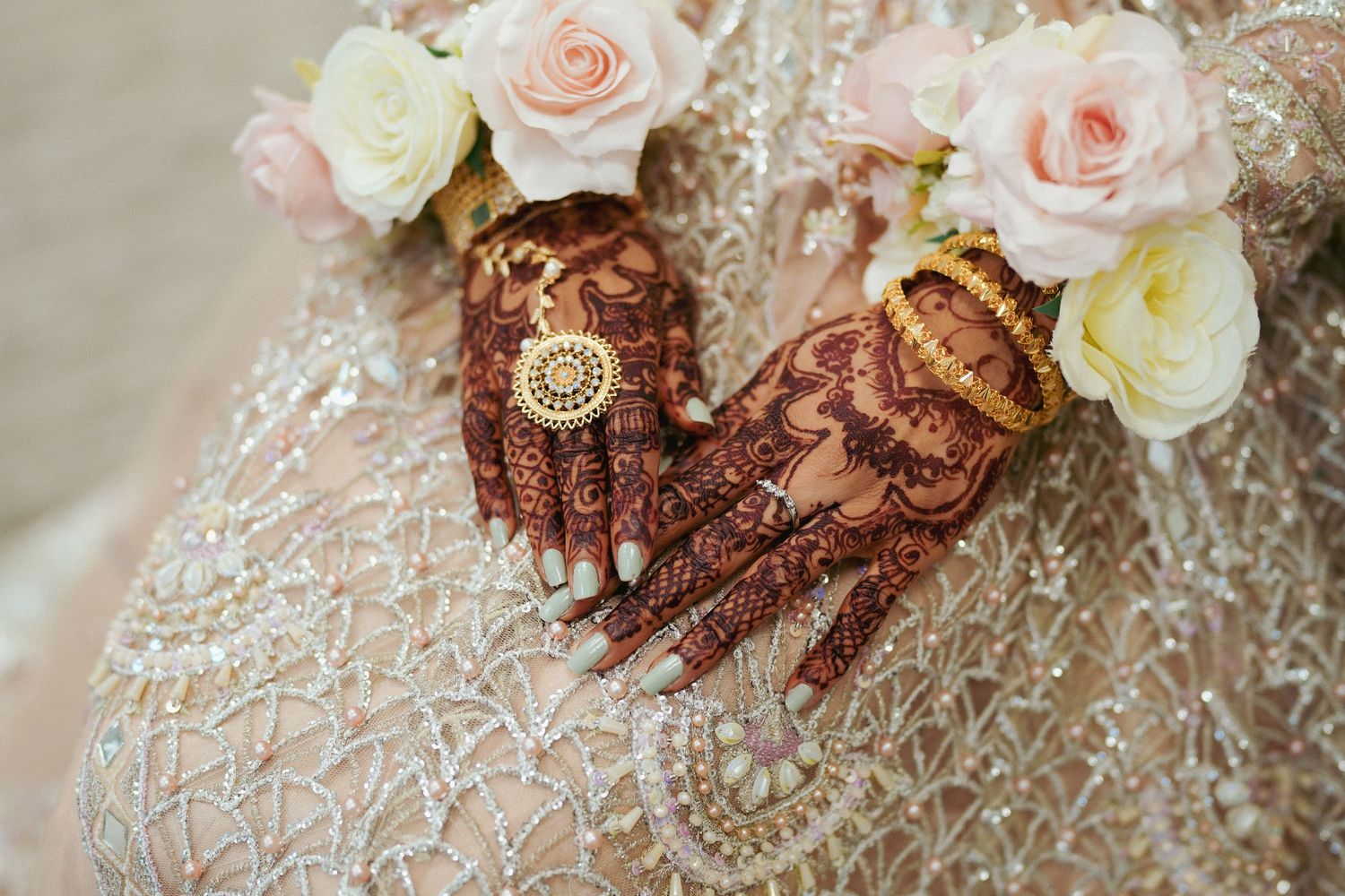 Close-up of delicate pink and white roses with intricate henna designs on hands.