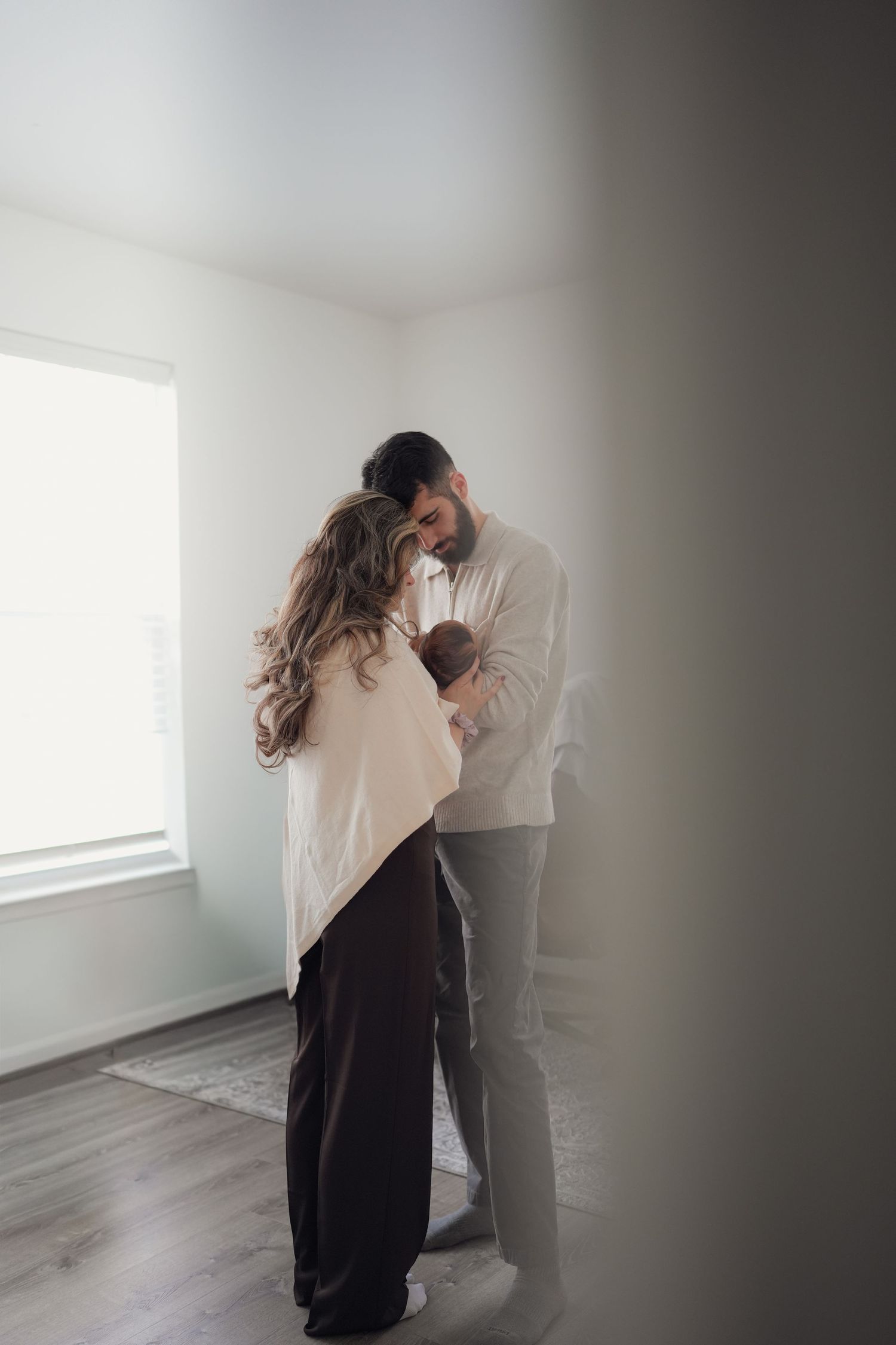 A couple embracing in an intimate moment against a minimalist white wall and grey flooring.