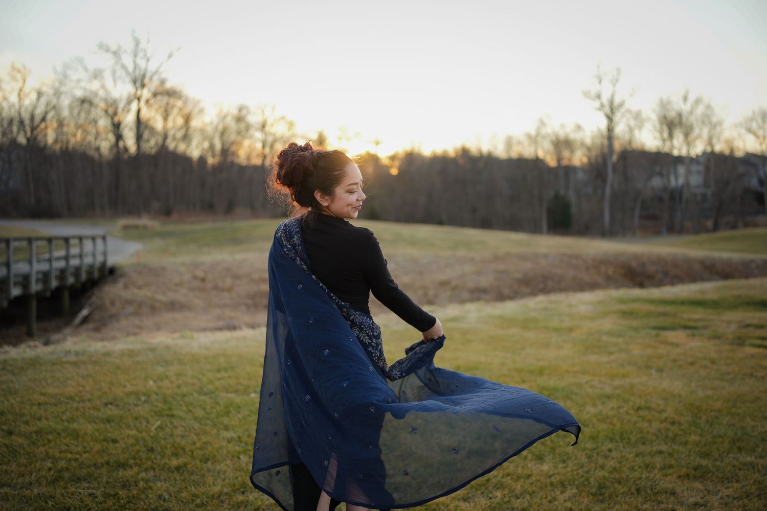 Person in denim jacket practicing yoga poses on black mat outdoors during sunset in grassy field.
