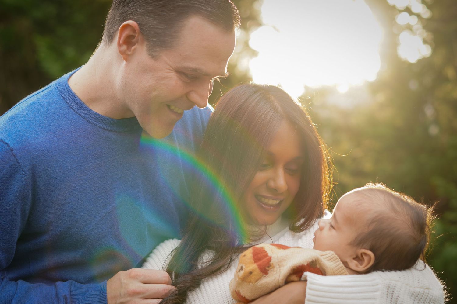 photography of a tender moment shared between a couple and baby in warm sunlight outdoors.