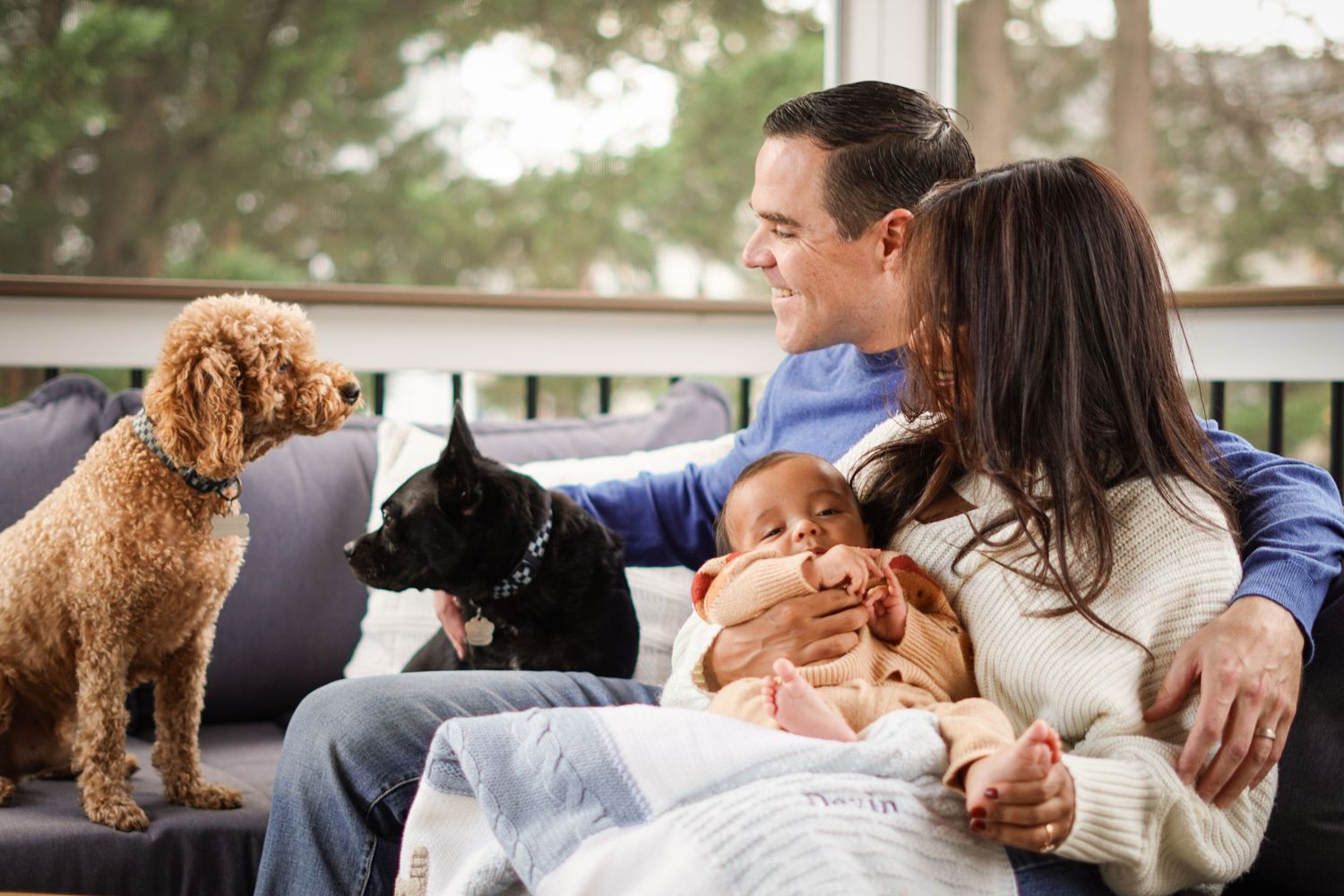 Family photoshoot relaxing together on couch with their pet dog and baby.