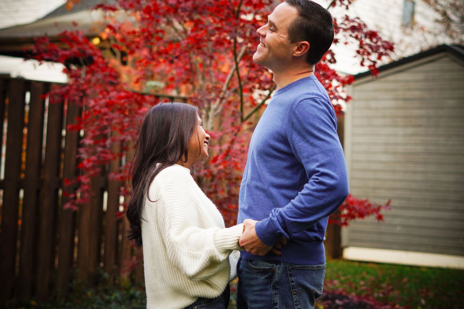 photography of  couple sharing a romantic moment among vibrant red autumn maple trees in a backyard setting.