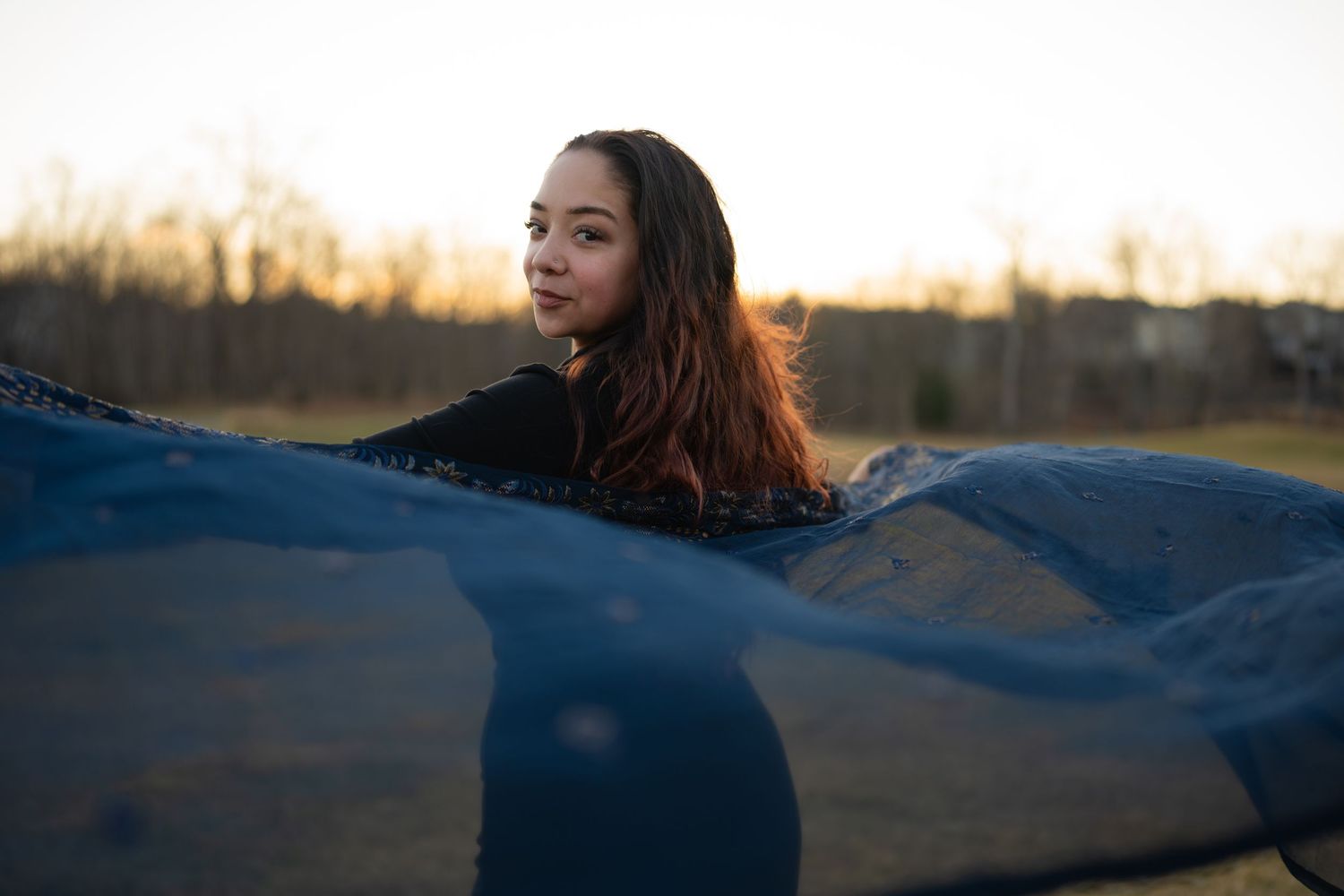 photoshoot of girl in fields wearing a dark blue dress and scarf flowing in the wind.