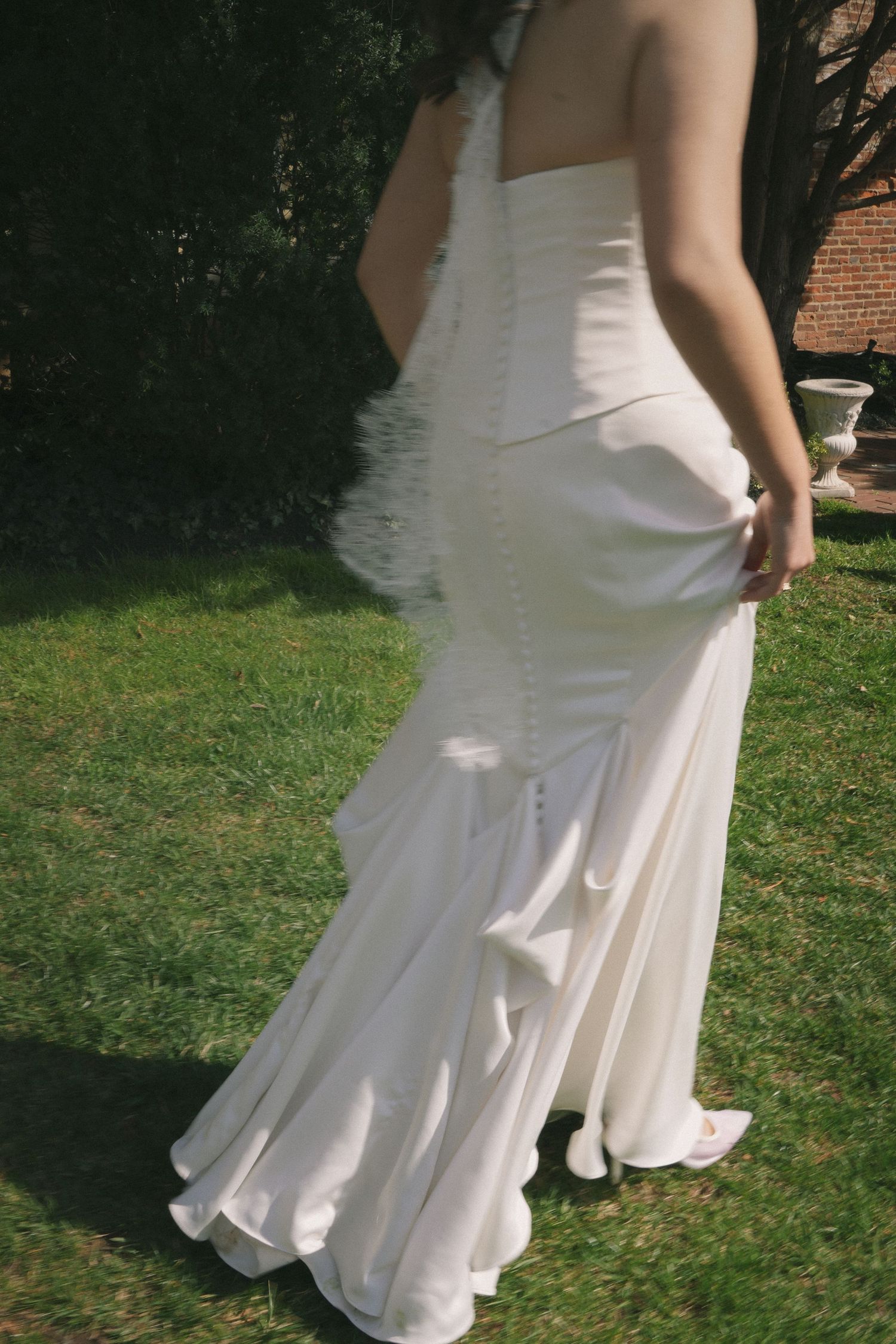 Elegant white mermaid wedding dress with button back detail, worn outdoors on green grass.