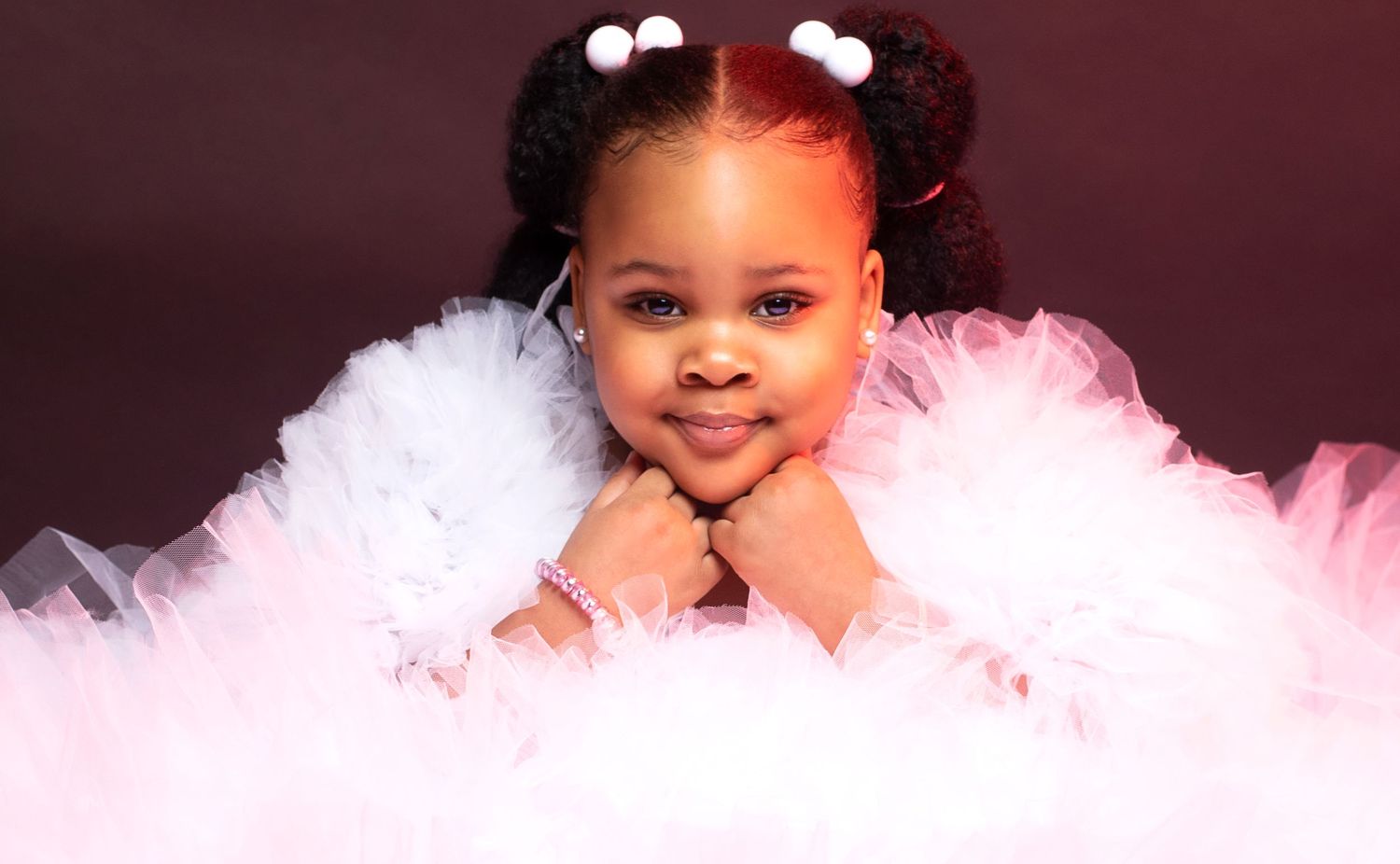 Adorable young girl in white and pink tutu dress posing with hands on chin.