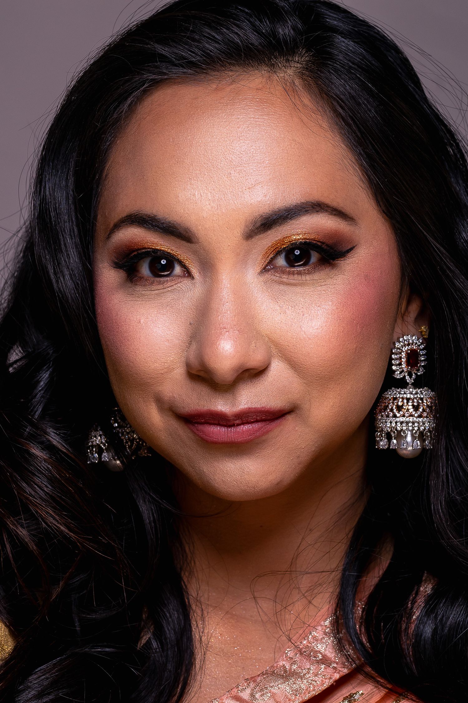 Close-up portrait of a woman wearing elegant silver earrings and warm eye makeup in traditional Indian attire.