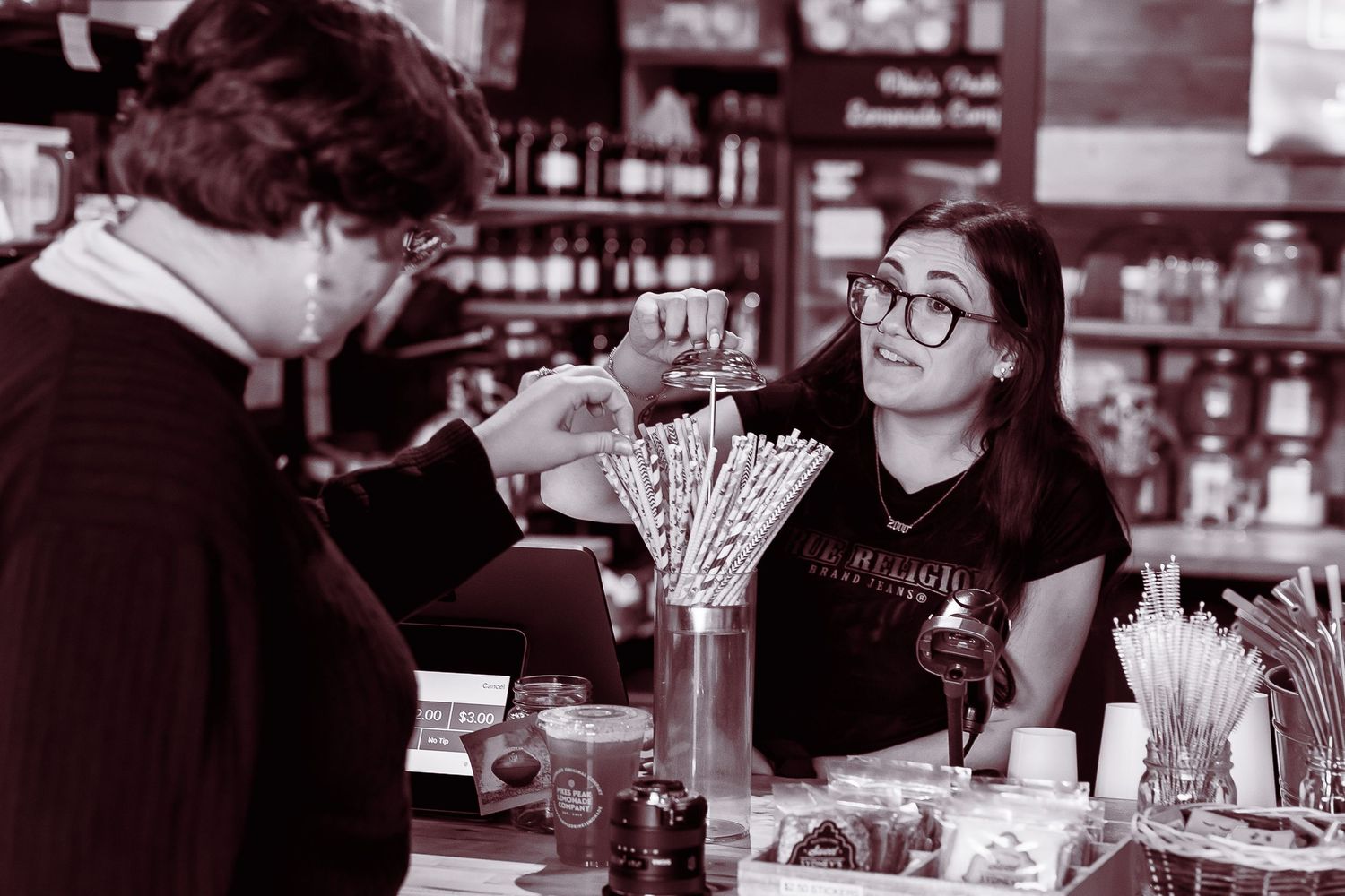 Barista in glasses serving drink to customer at vintage cafe counter in black and white.