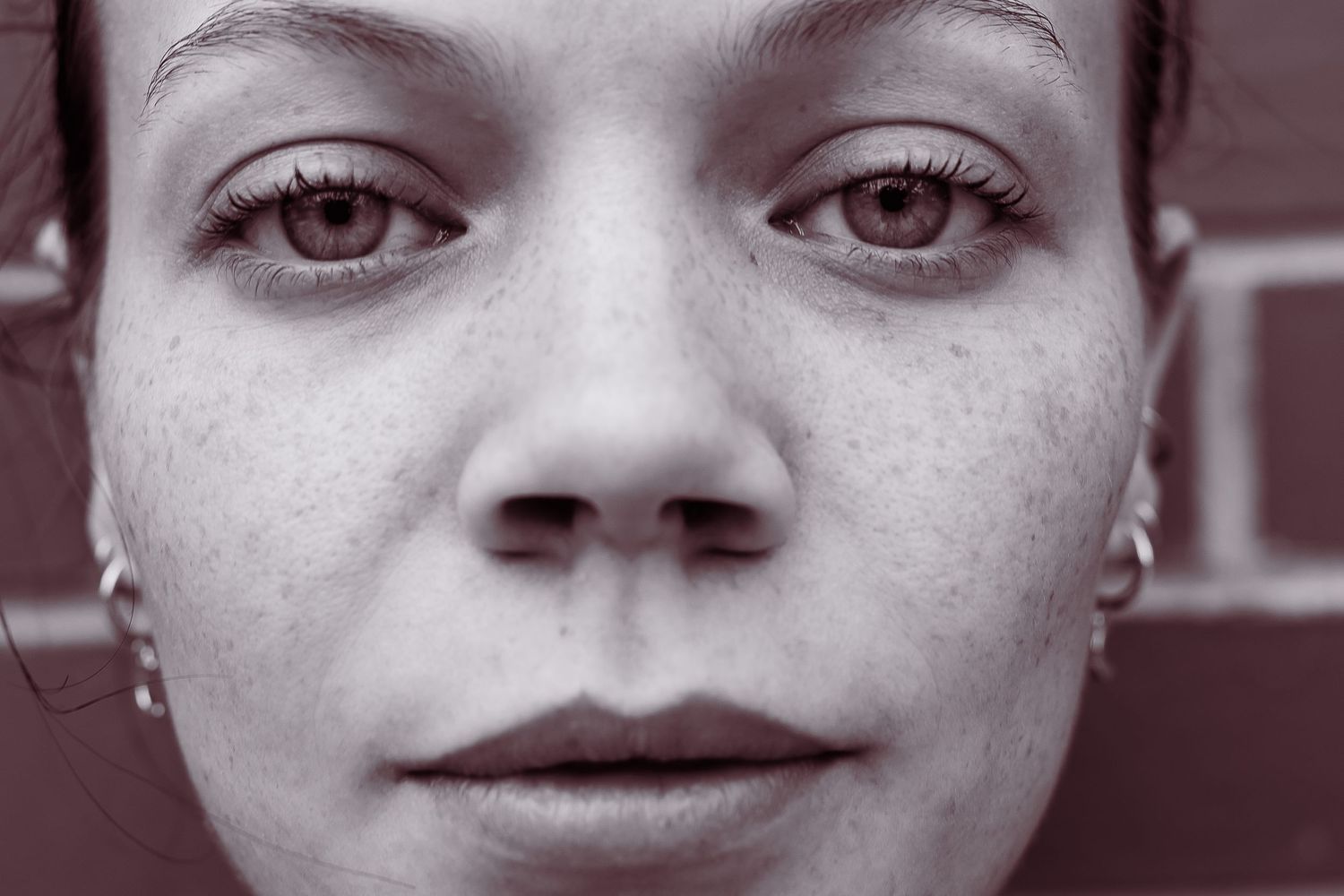 Close-up black and white portrait of a young woman with freckles and brown eyes wearing small hoop earrings.