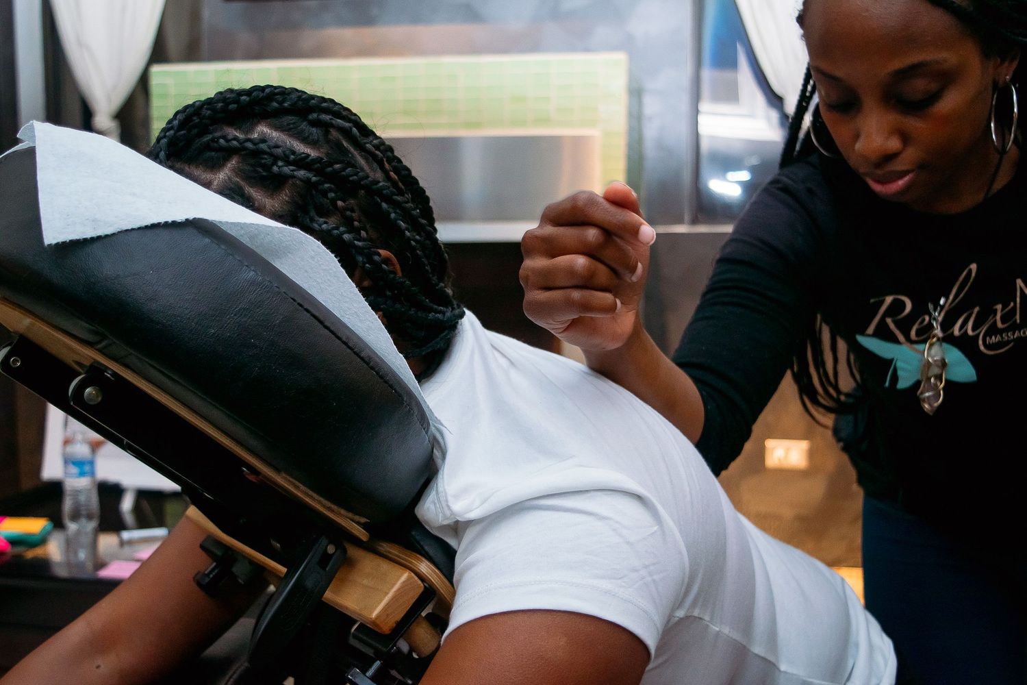 Massage therapist performing arm and shoulder stretch on seated client.