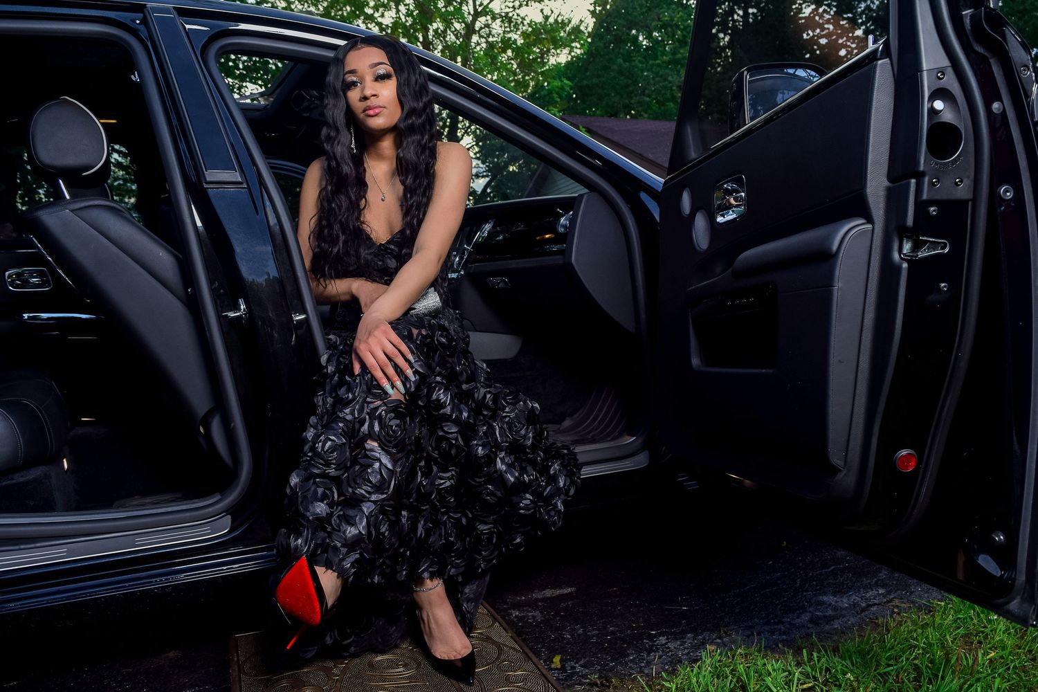 Woman in black floral gown sitting in luxury car door.