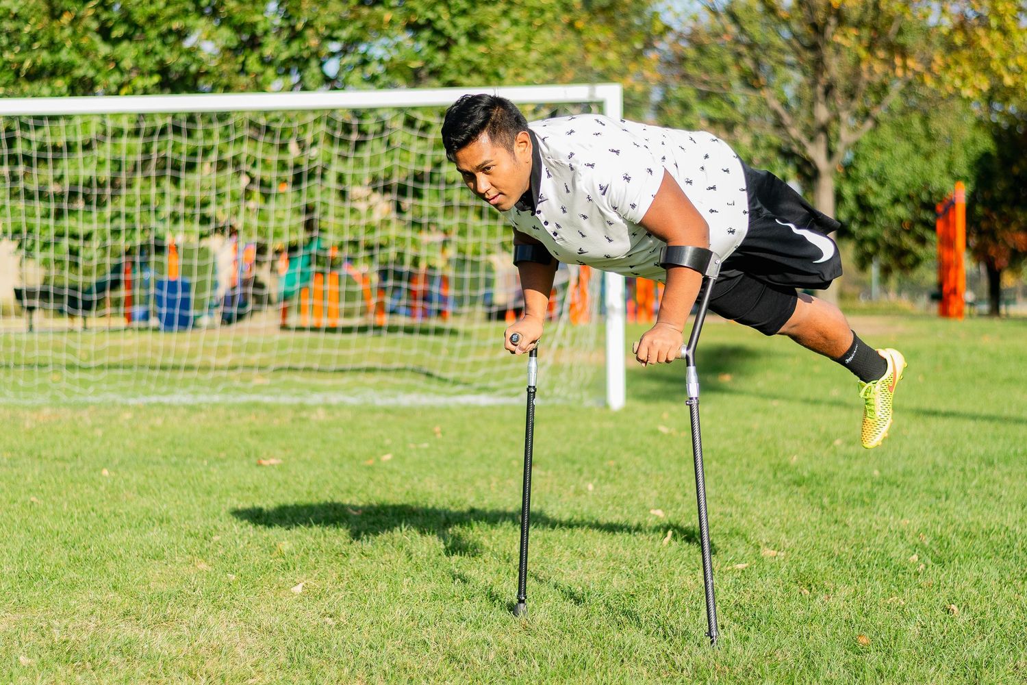 Athletic amputee man performing horizontal plank pose on crutches on a green soccer field.