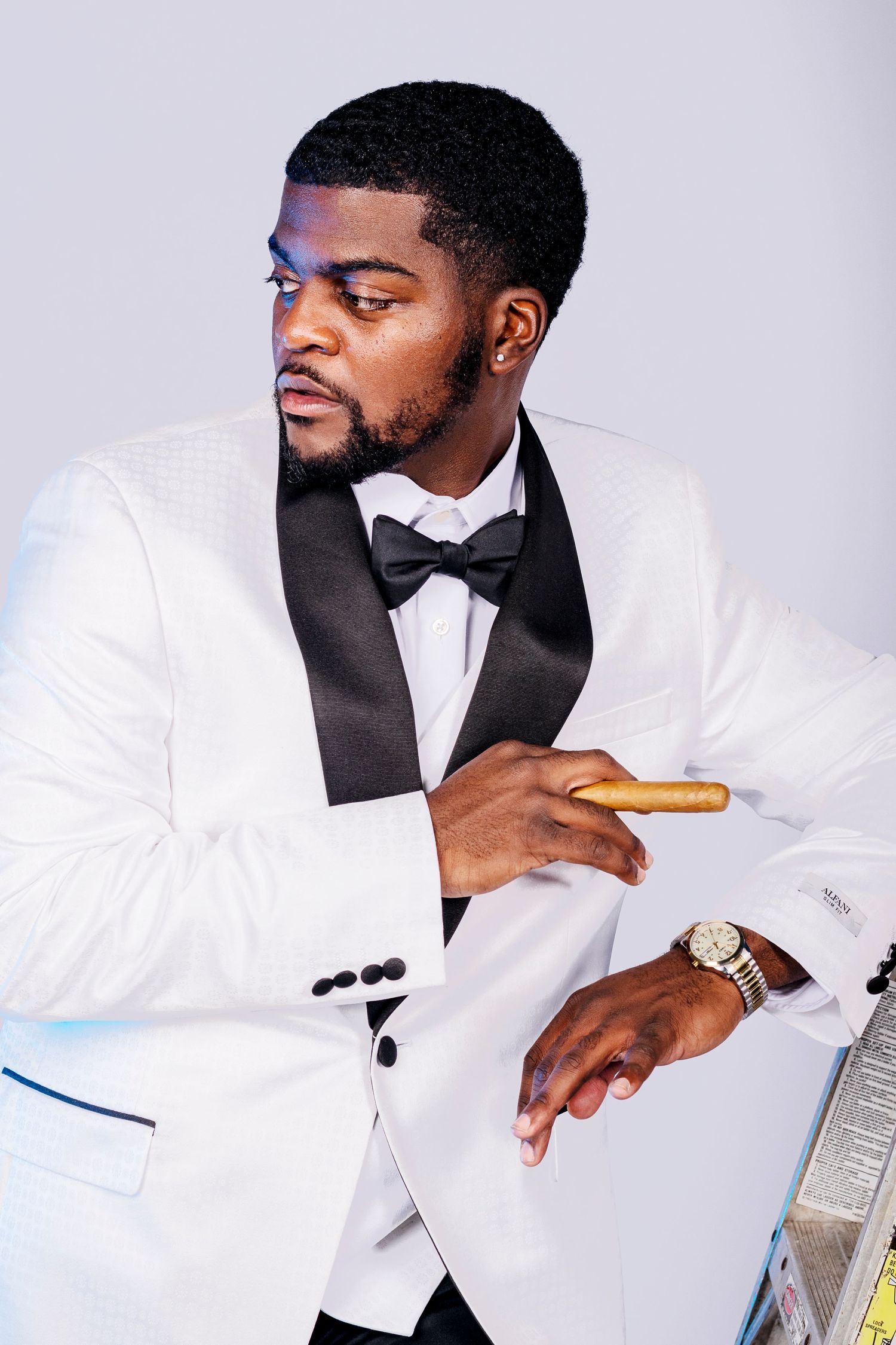 Stylish man in a white tuxedo jacket holding a cigar while leaning on a surface.