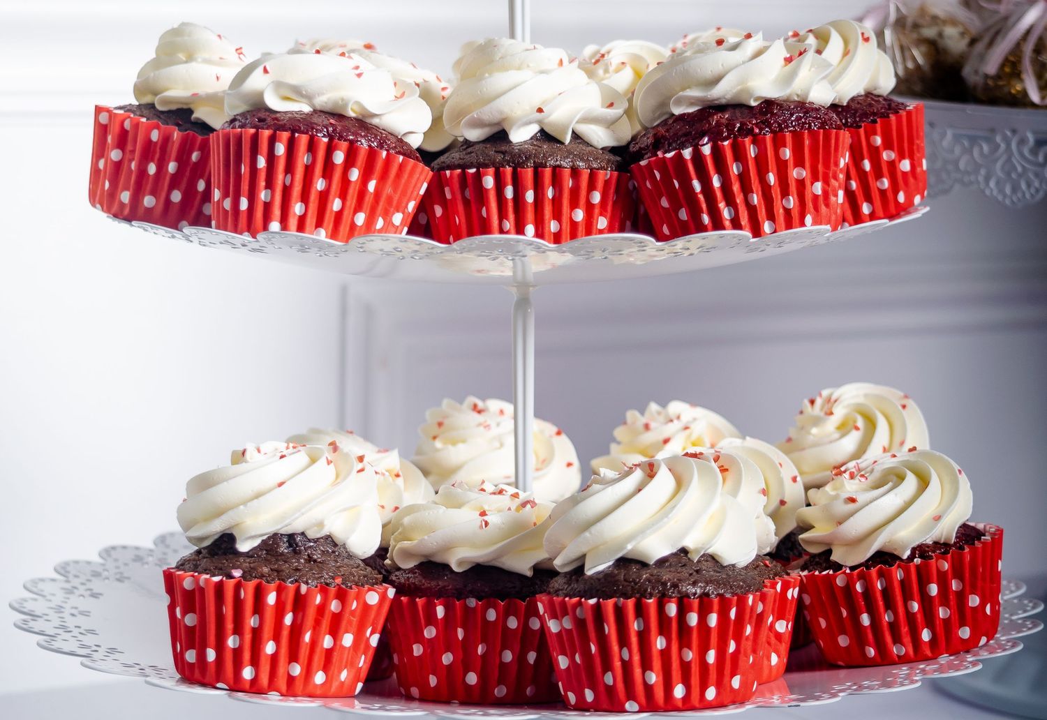 Two-tier dessert stand filled with chocolate cupcakes topped with white frosting in red polka dot liners.