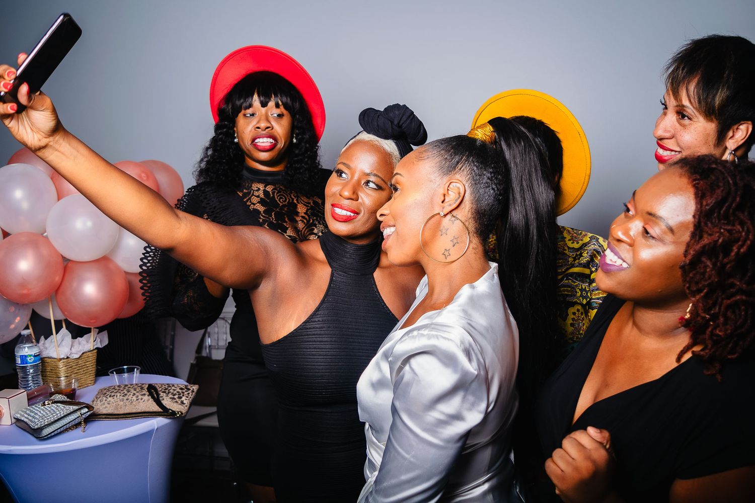 Group of women taking a selfie together at a festive party with balloons in background.