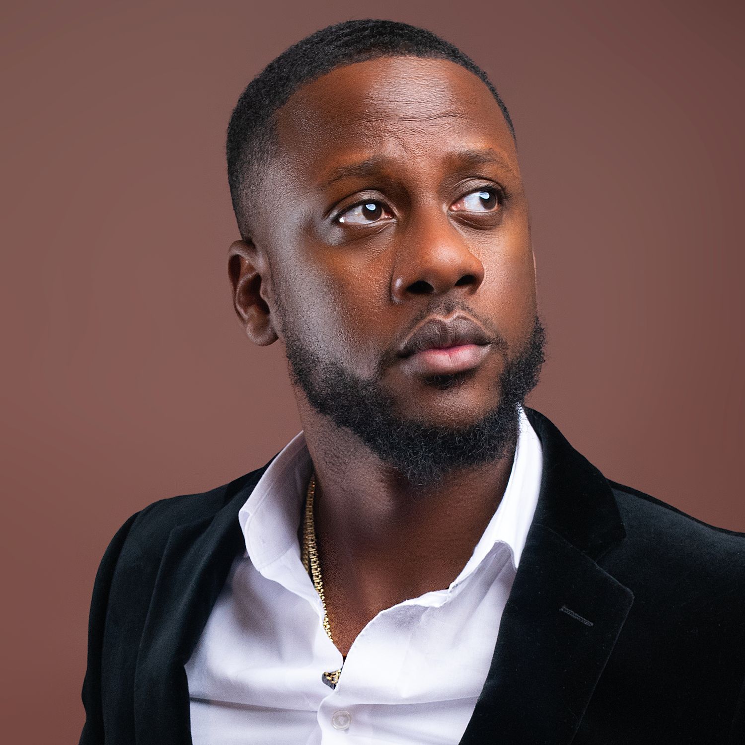 Stylish Black man in a black blazer and white shirt with a gold chain looking upward.