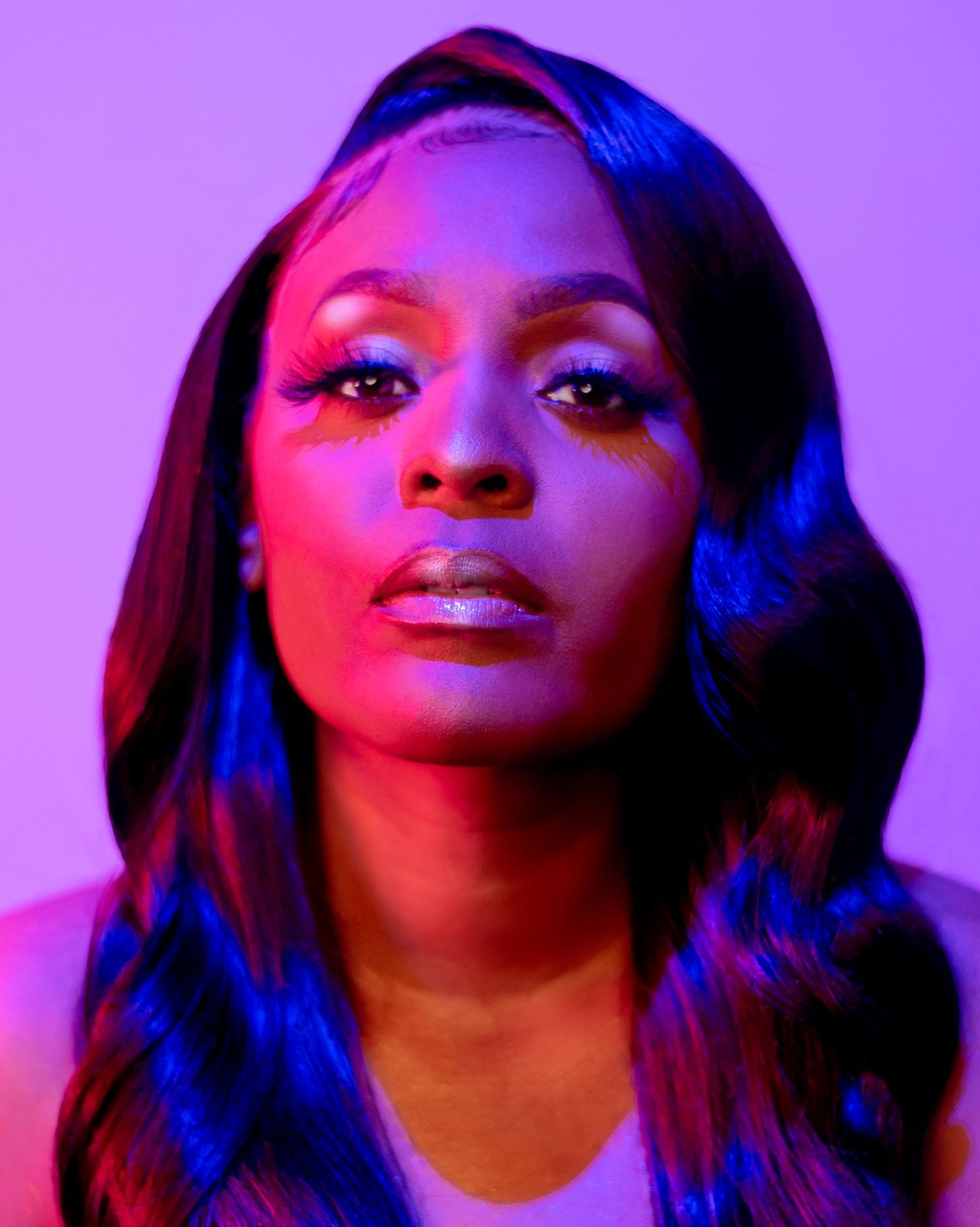 Woman with dramatic blue eye makeup and glossy lips under vibrant purple and red neon lighting.