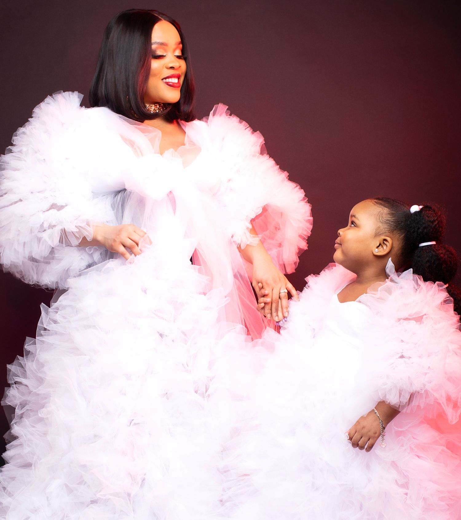 Mother and daughter in matching white ruffled tulle dresses smiling together in studio portrait.