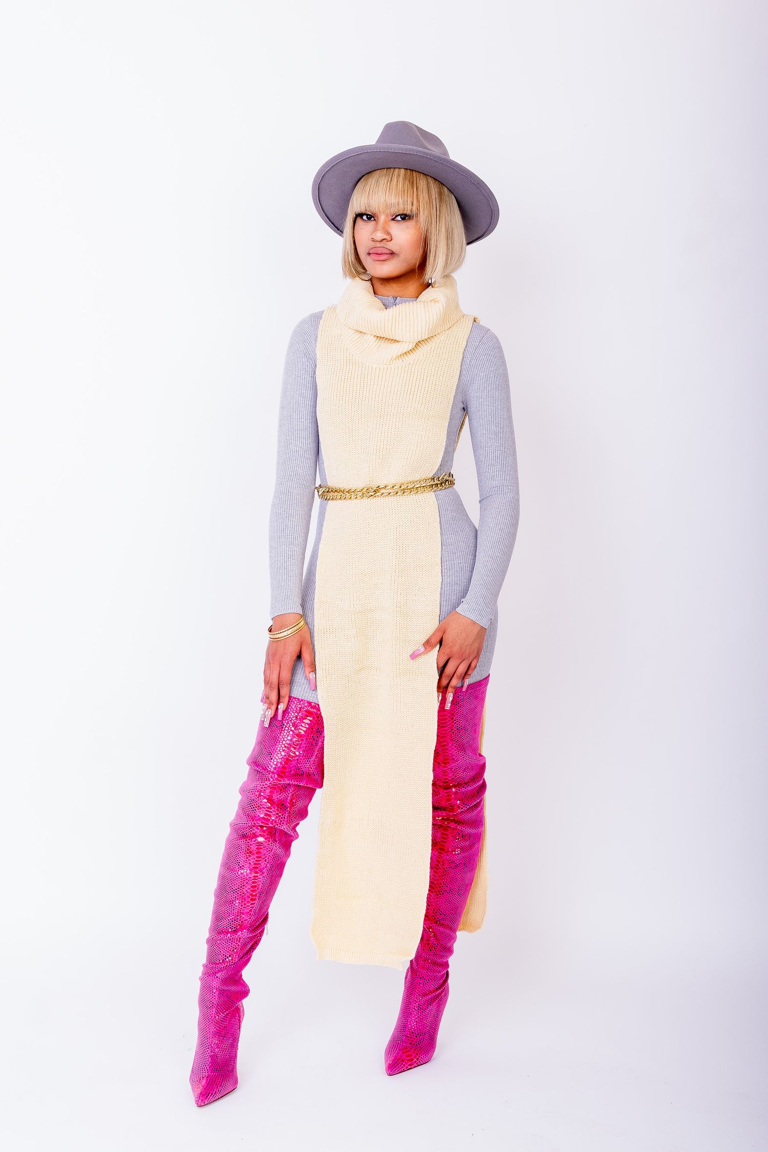 Woman in cream vest dress with gray turtleneck, gold belt, pink thigh-high boots, and gray wide-brim hat.