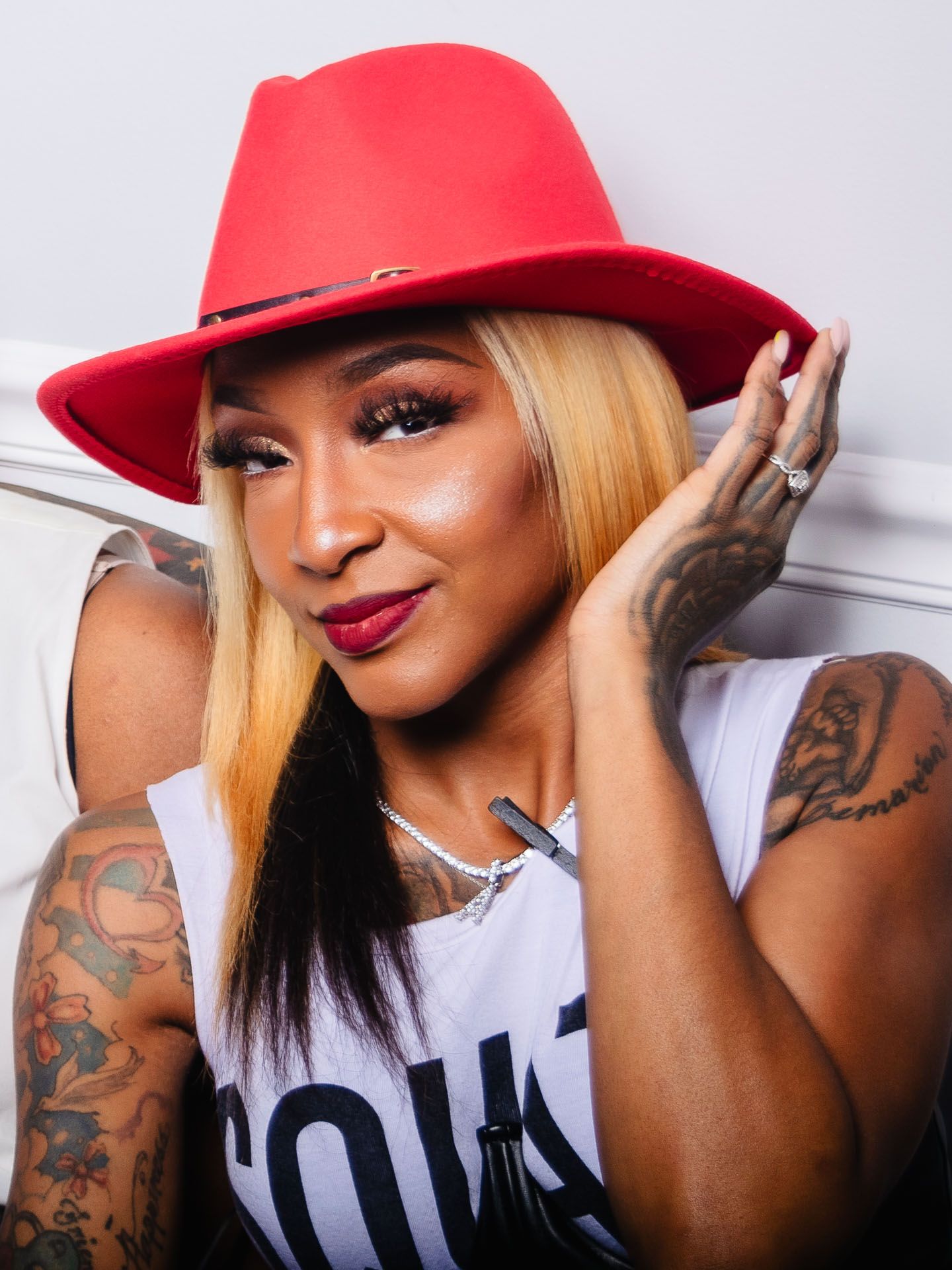 Portrait of a tattooed woman wearing a red hat and white graphic tee, posing casually.