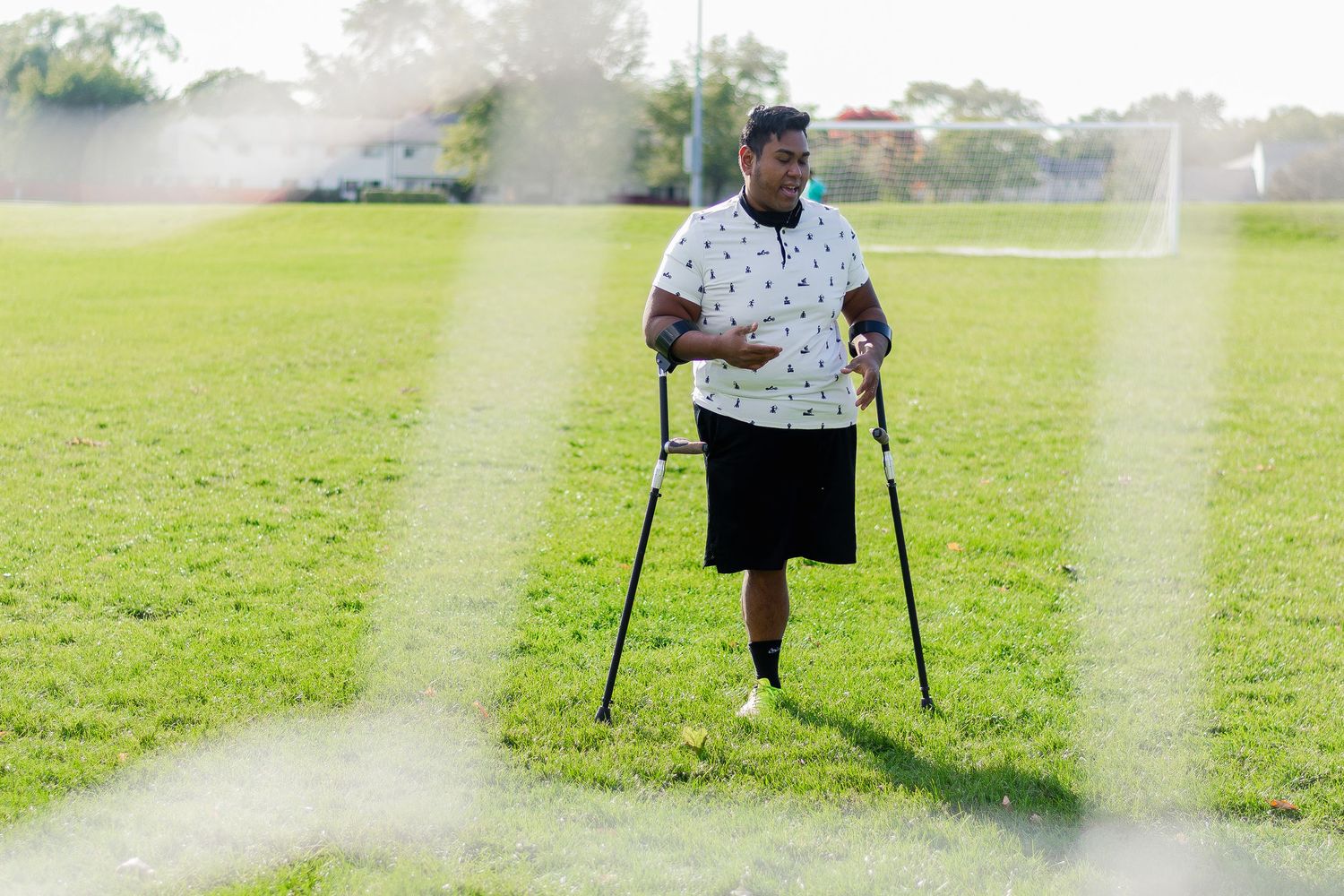 Man with prosthetic leg using crutches walking on a green grass field outdoors.