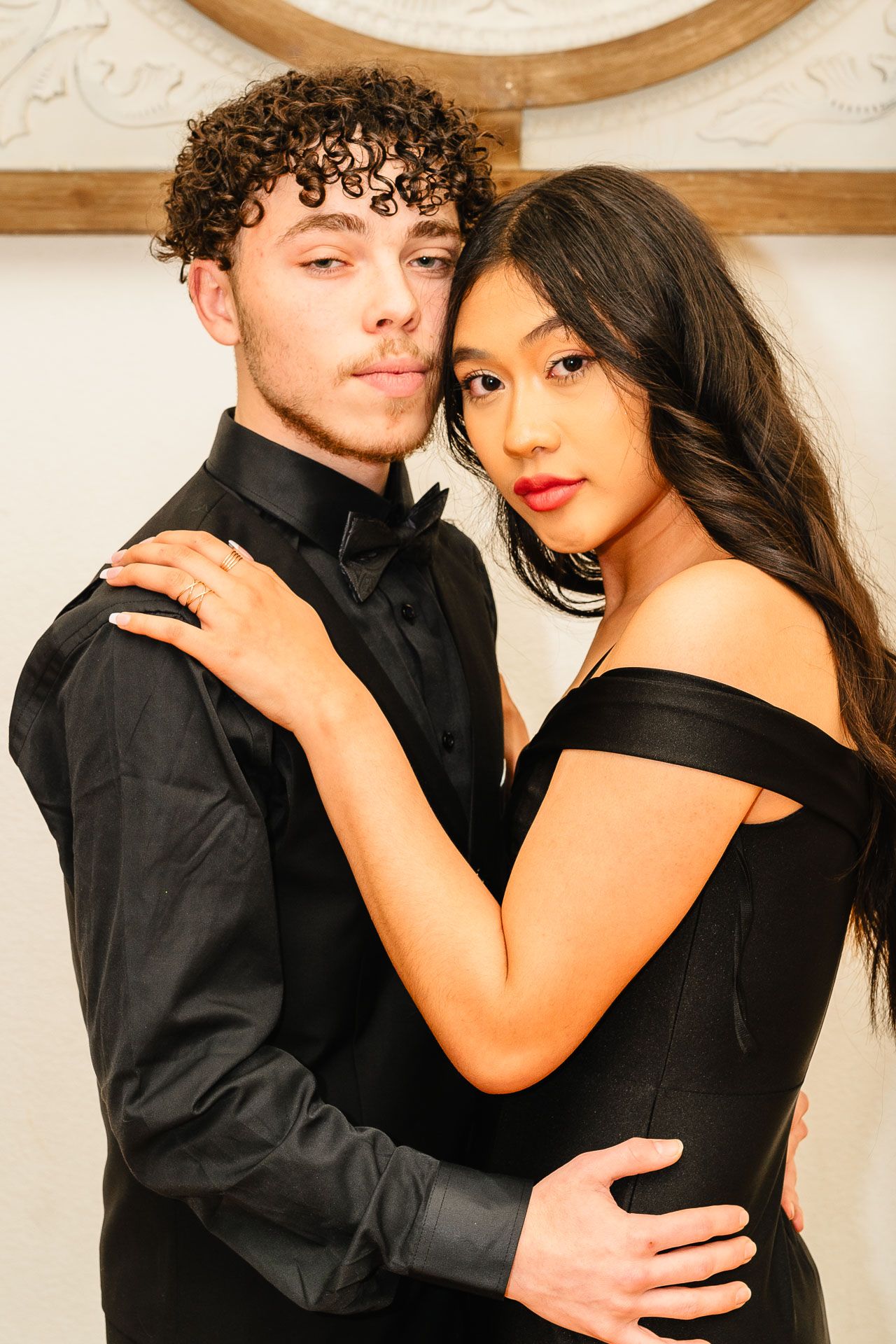 Young couple in black formalwear posing closely for prom photo.