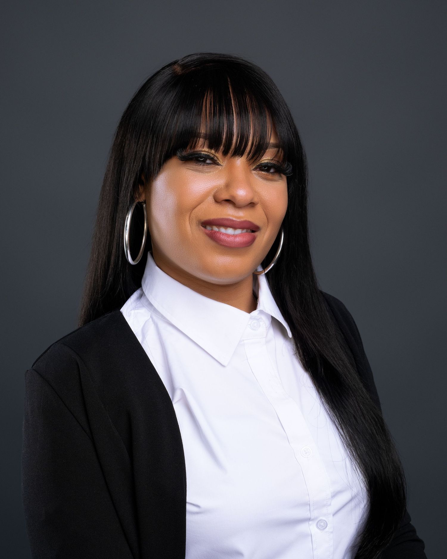 Professional Black woman with straight black hair and bangs smiles in black blazer and white shirt.