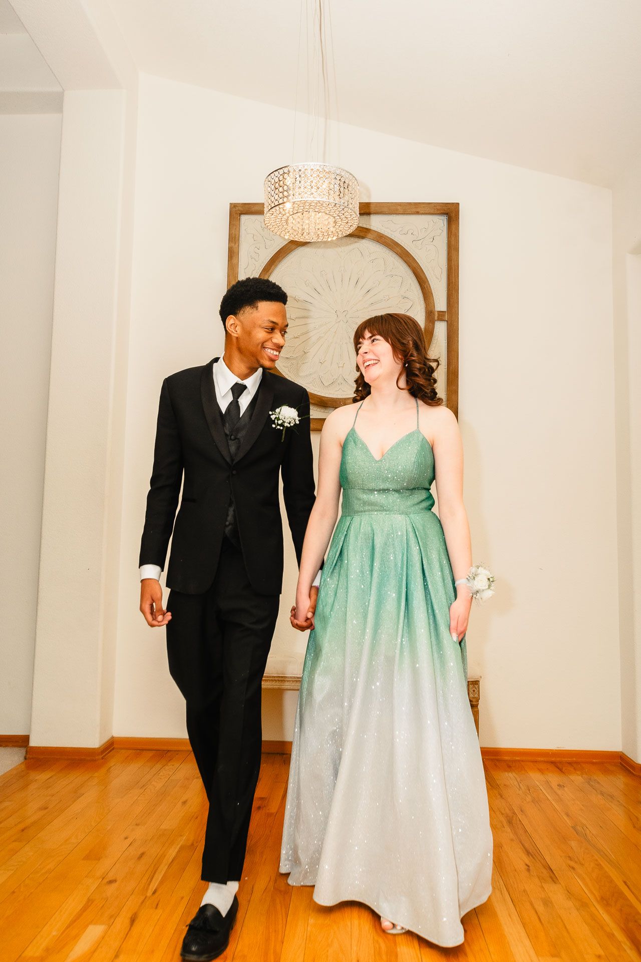 Smiling prom couple walking hand in hand in formal wear.