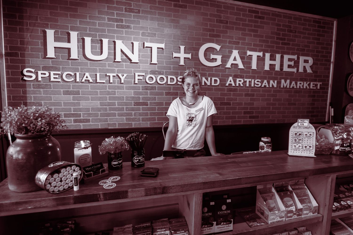 Smiling woman behind the counter at Hunt and Gather Specialty Foods and Artisan Market in black and white.