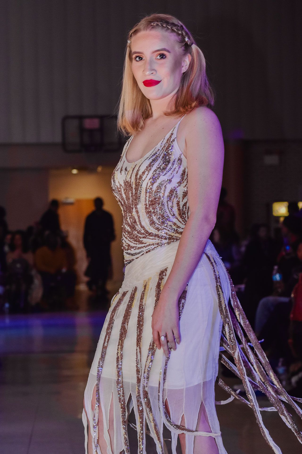 Woman in sequined white fringe dress with red lips posing at fashion show event.