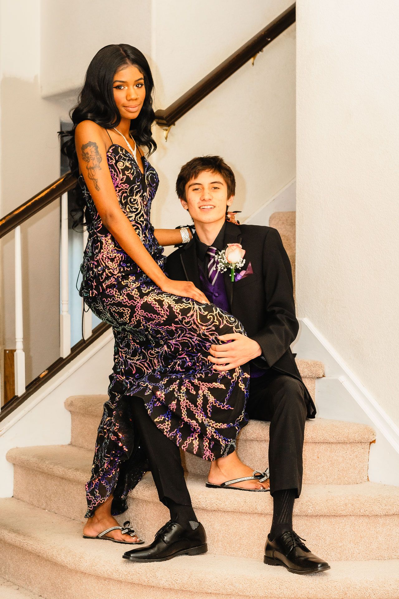 Prom couple posing on staircase in elegant formal attire.