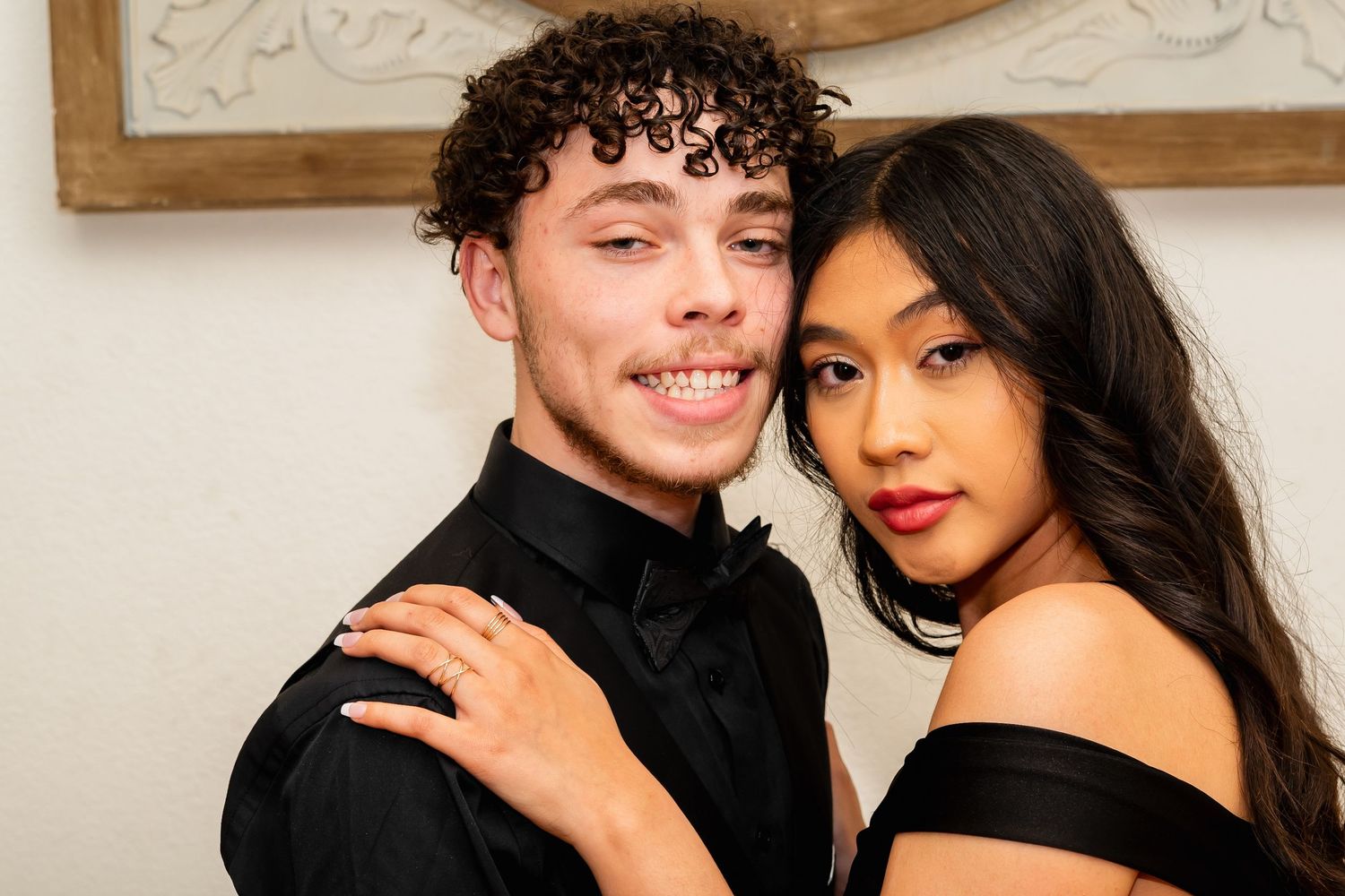 Smiling young couple dressed in formal black attire posing together at a special event.