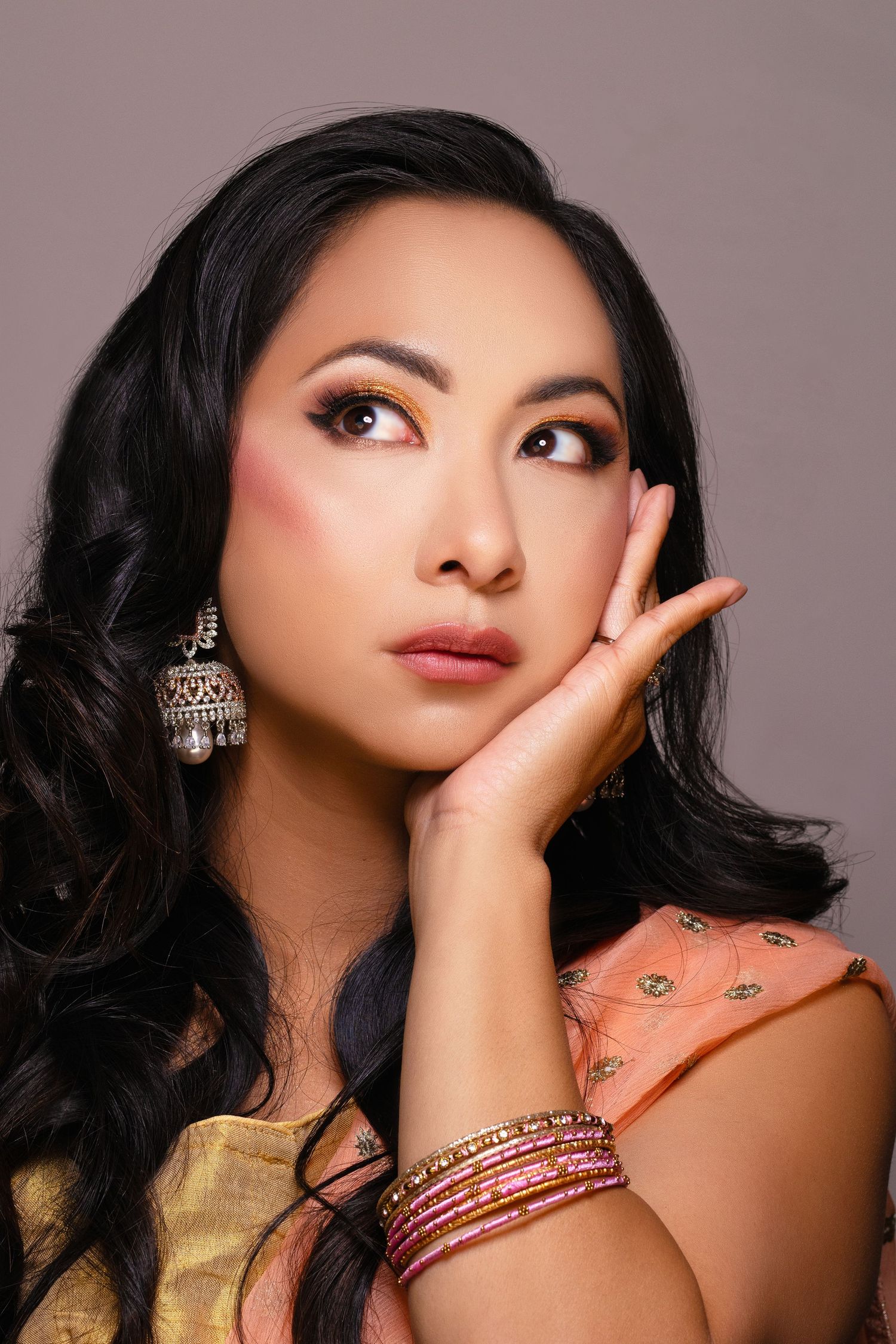 Woman in Indian attire with colorful bangles and ethnic earrings wearing warm-toned makeup.