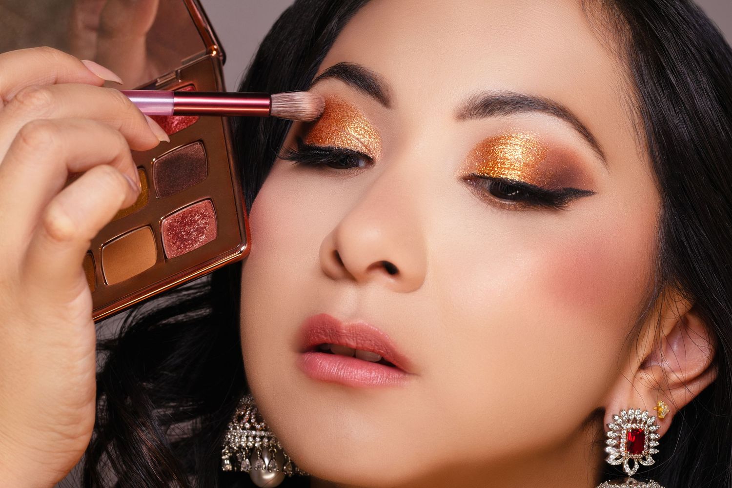 Close-up of woman receiving glamorous gold and orange eyeshadow makeup application with brush.