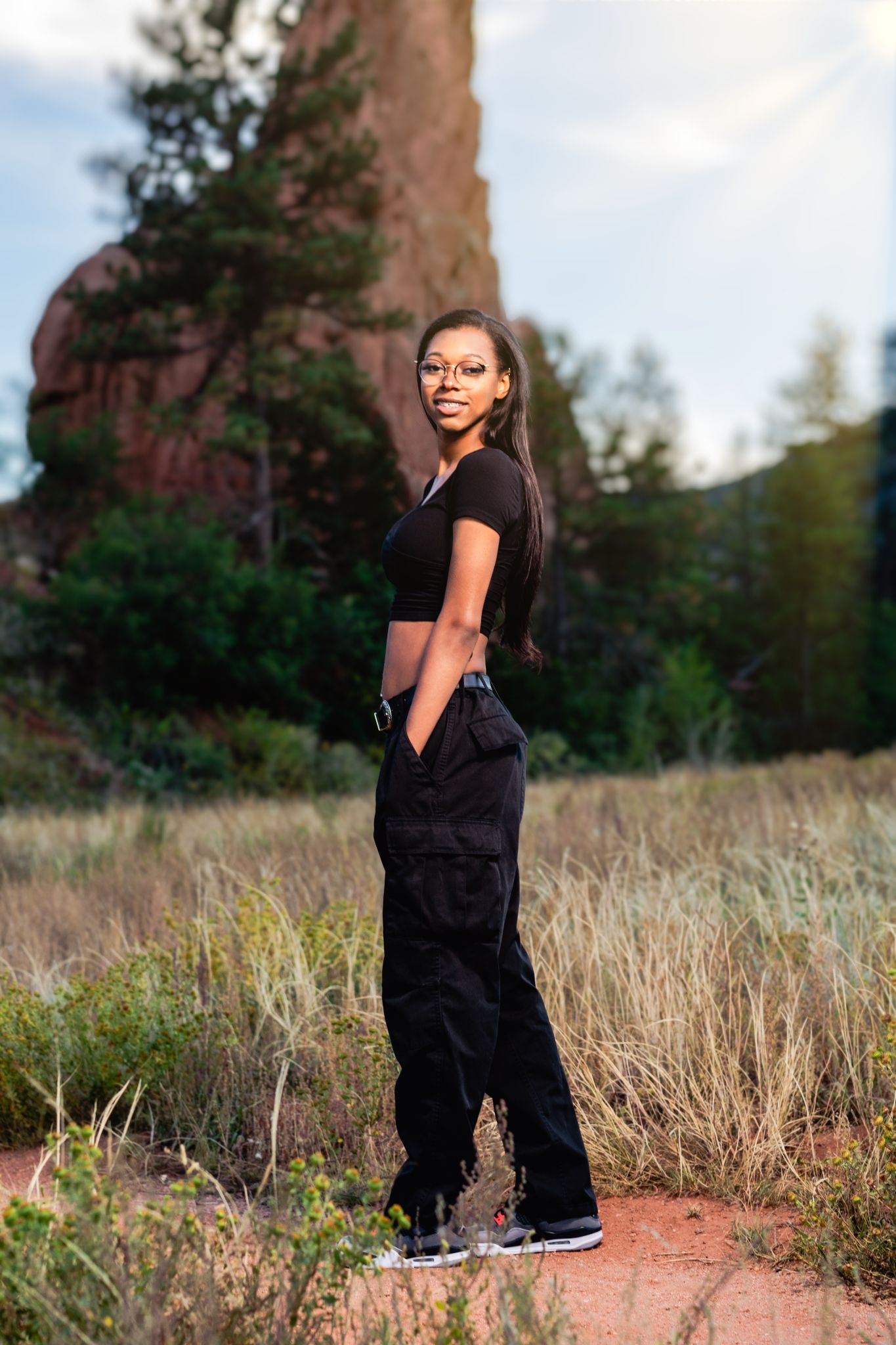 Young Black woman in black crop top and cargo pants posing in a scenic red rock landscape.