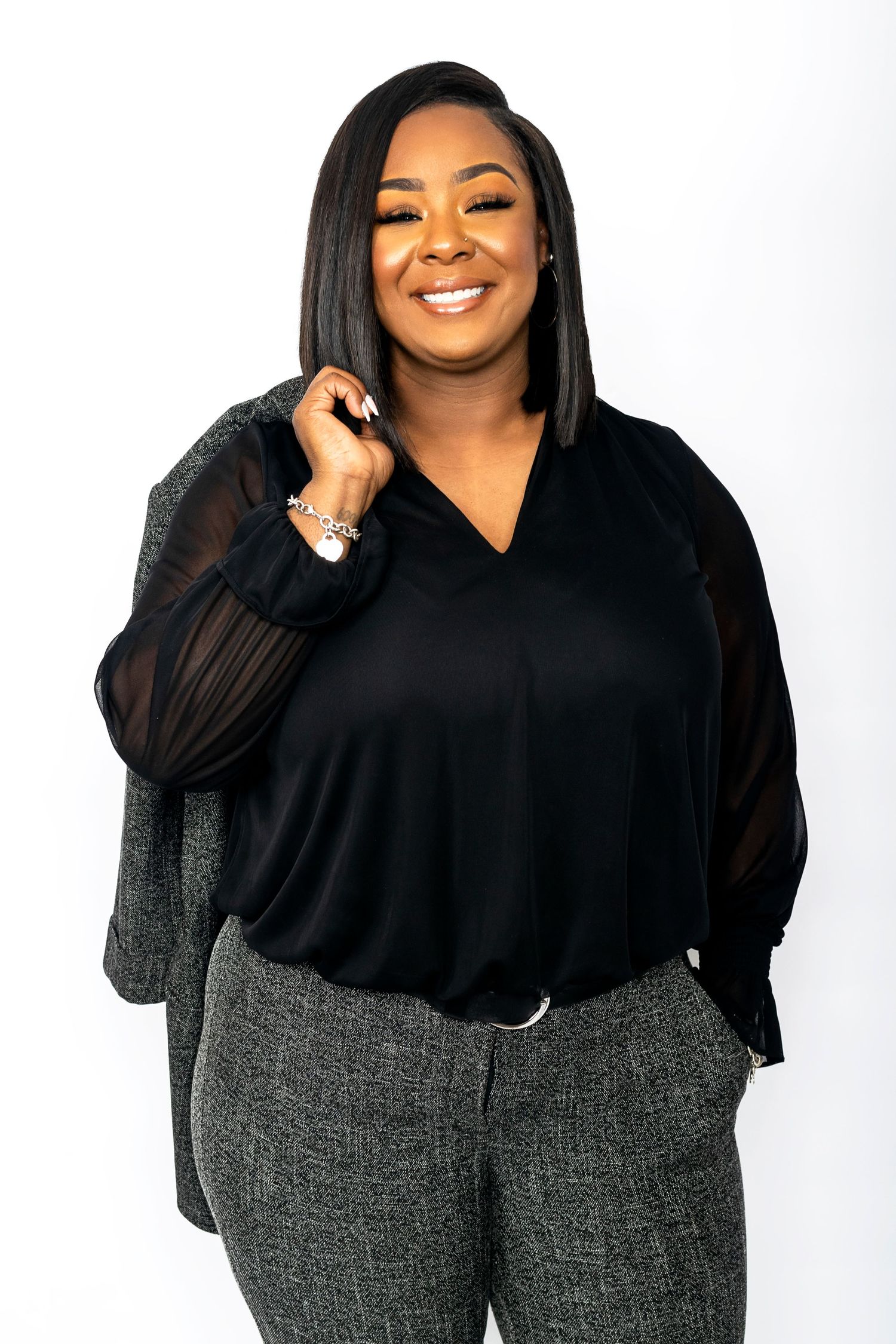 Smiling plus-size woman in black blouse and gray plaid pants posing on white background.