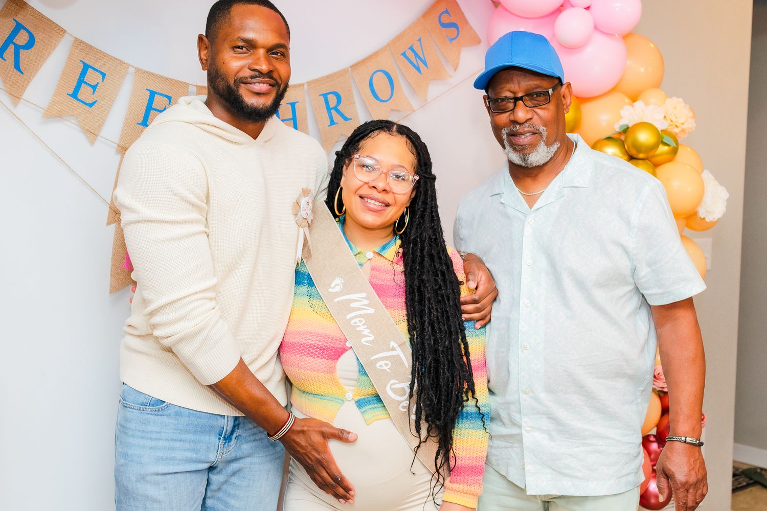 Three Black adults smiling together at a basketball-themed baby shower with balloon decorations.
