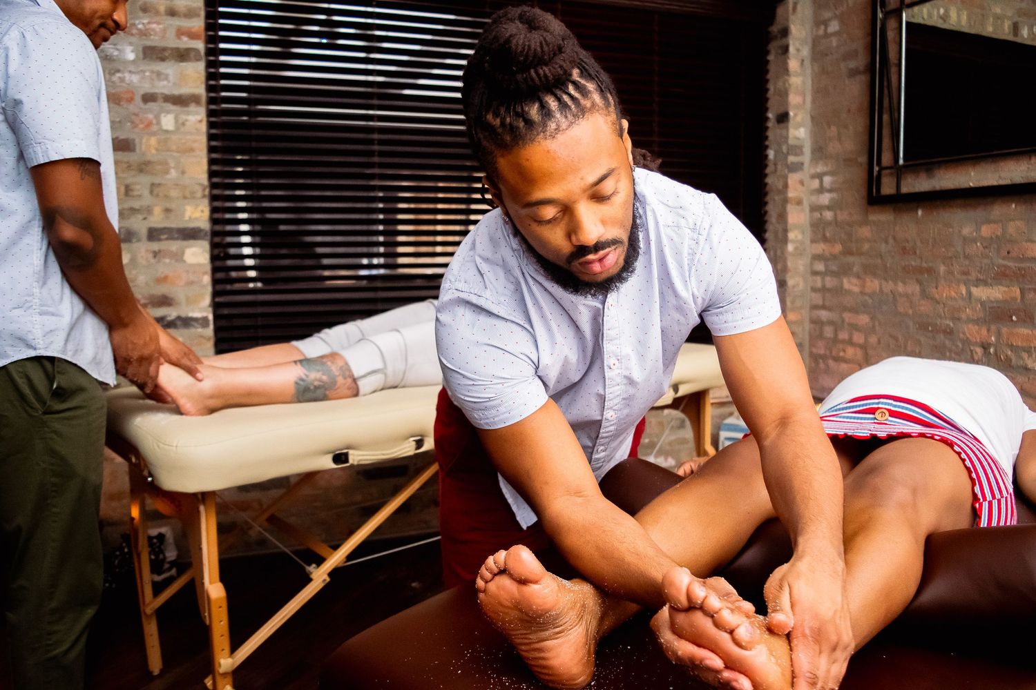Male massage therapist performing foot massage on client at massage table.