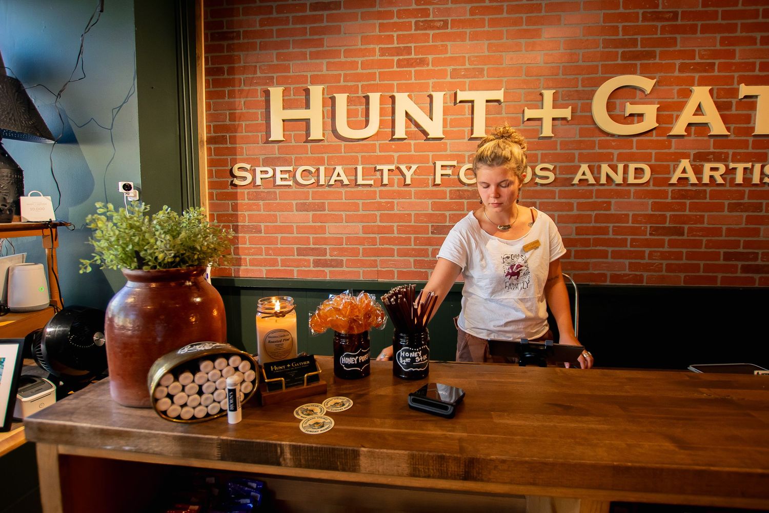 A woman stands behind a wooden counter at Hunt and Gather Specialty Foods store.