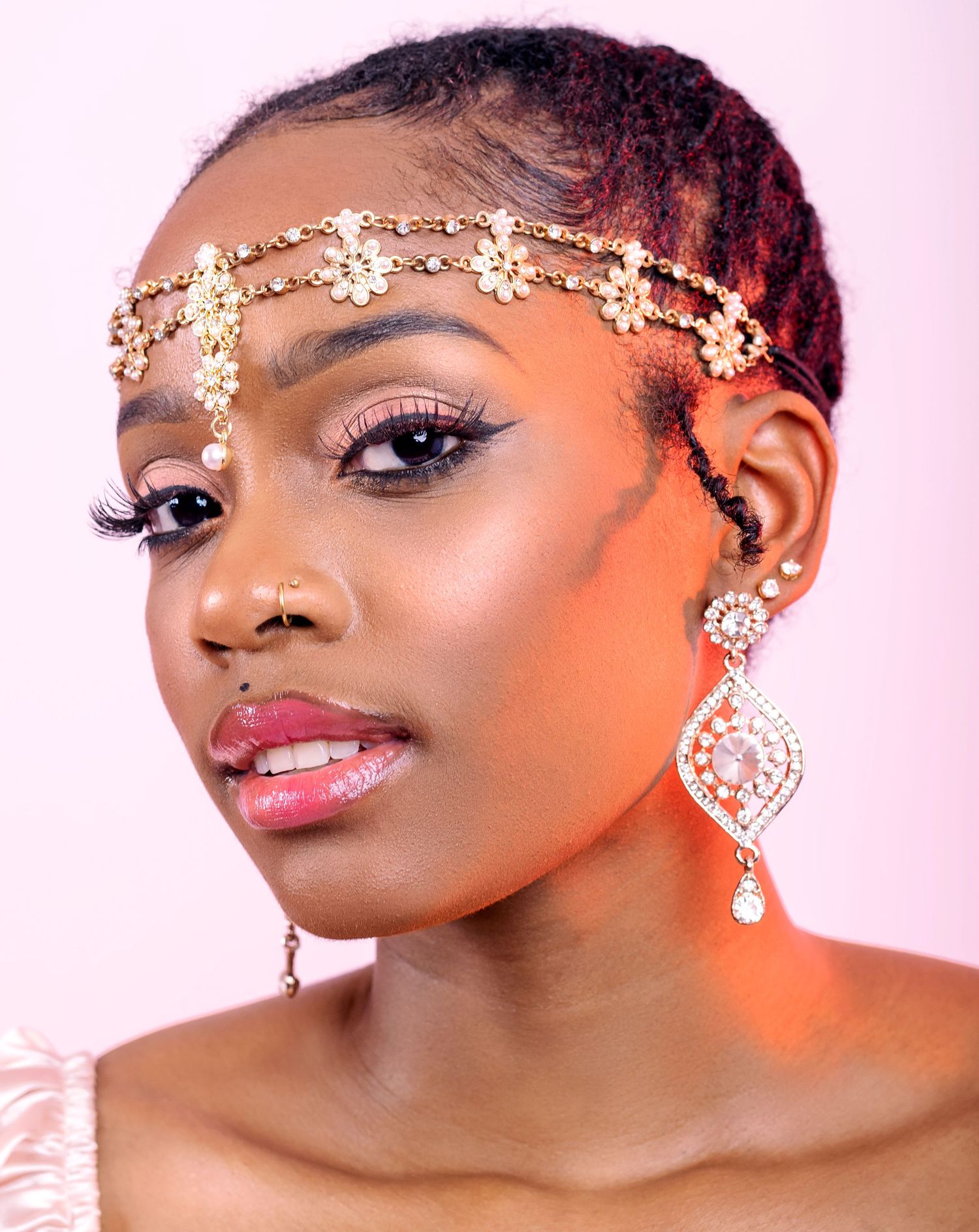 Woman wearing gold floral hair chain and crystal drop earrings with elegant bridal makeup.