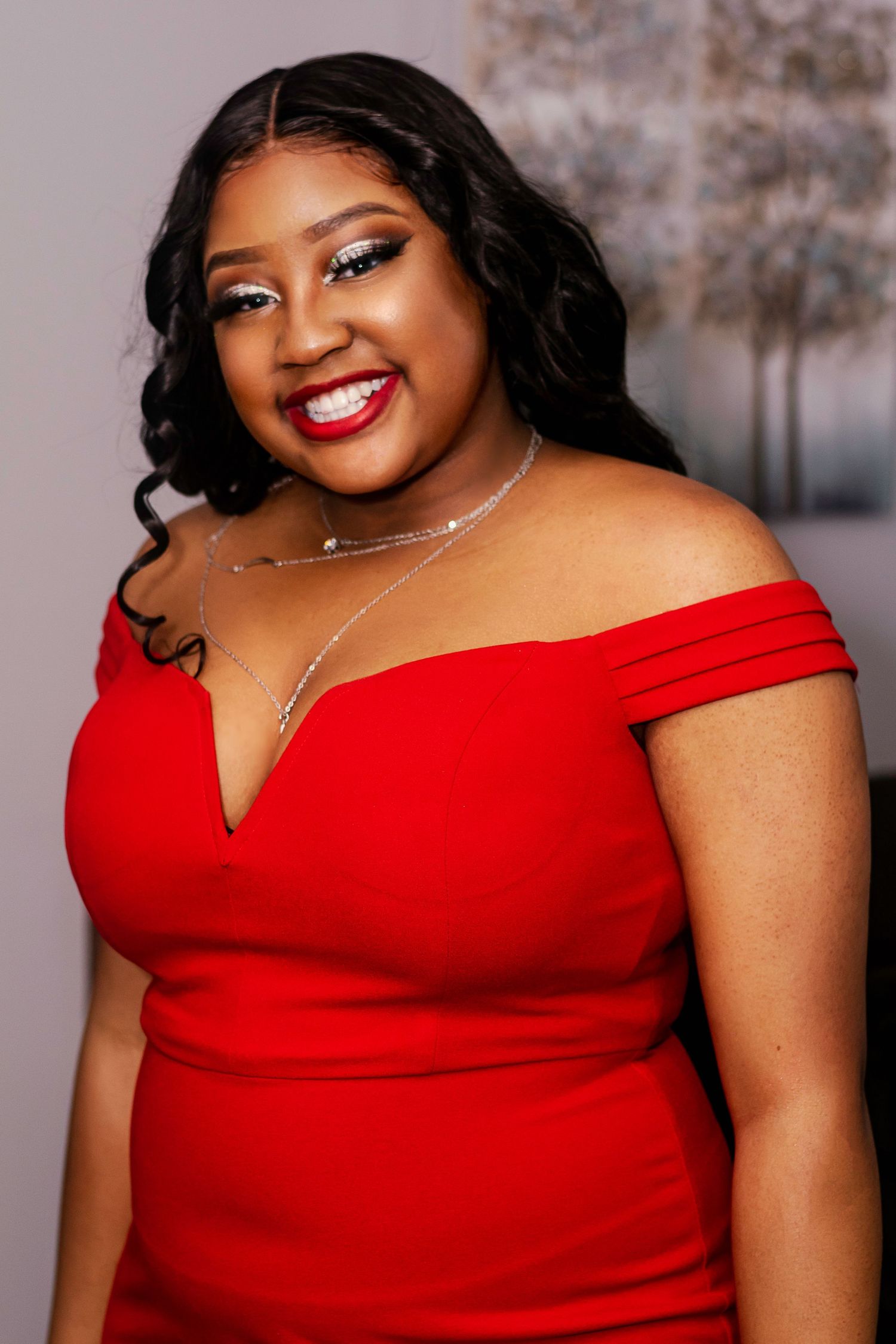 Woman smiling in red off-shoulder dress with silver necklace.