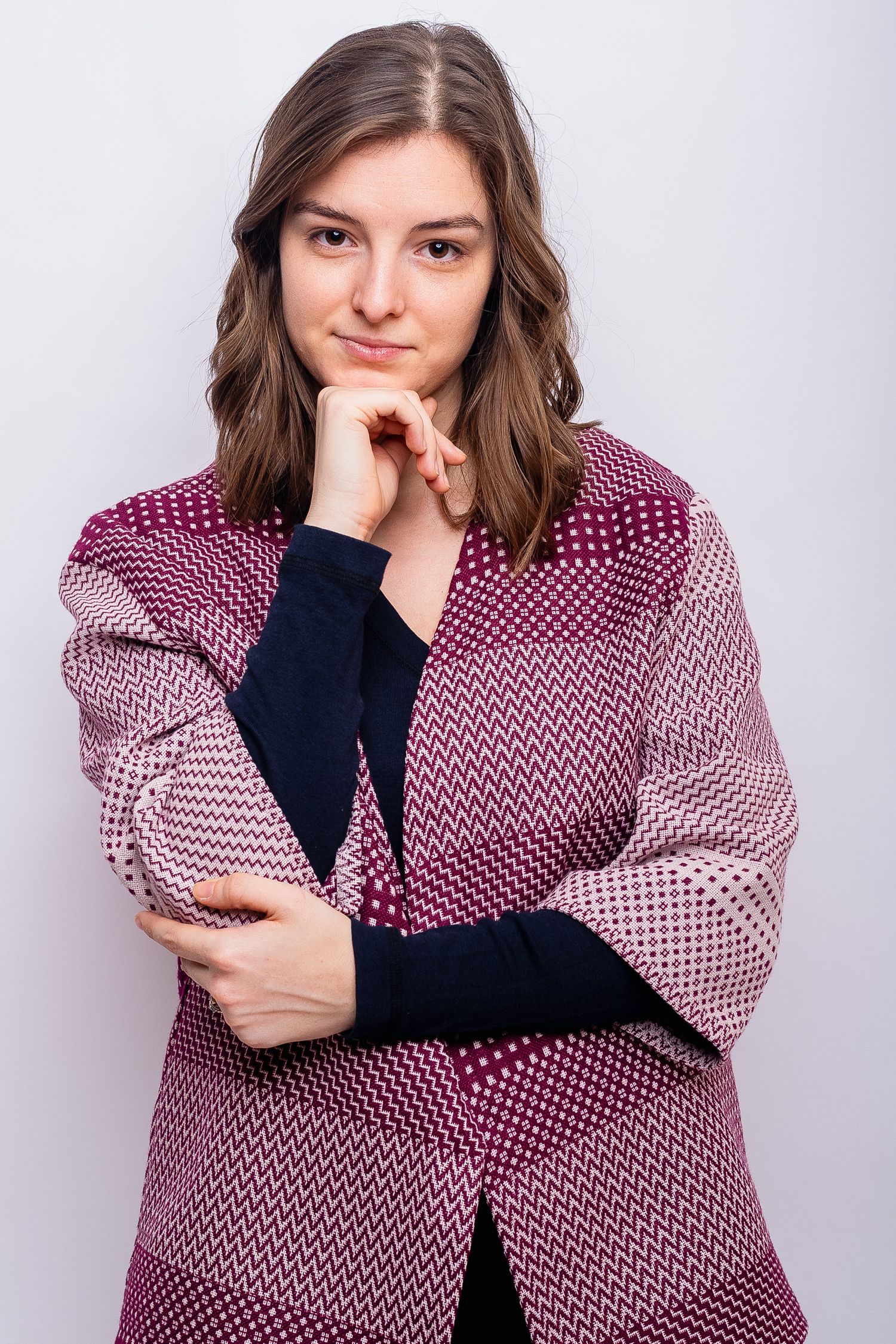 Woman in a burgundy geometric patterned coat posing thoughtfully with hand on chin.